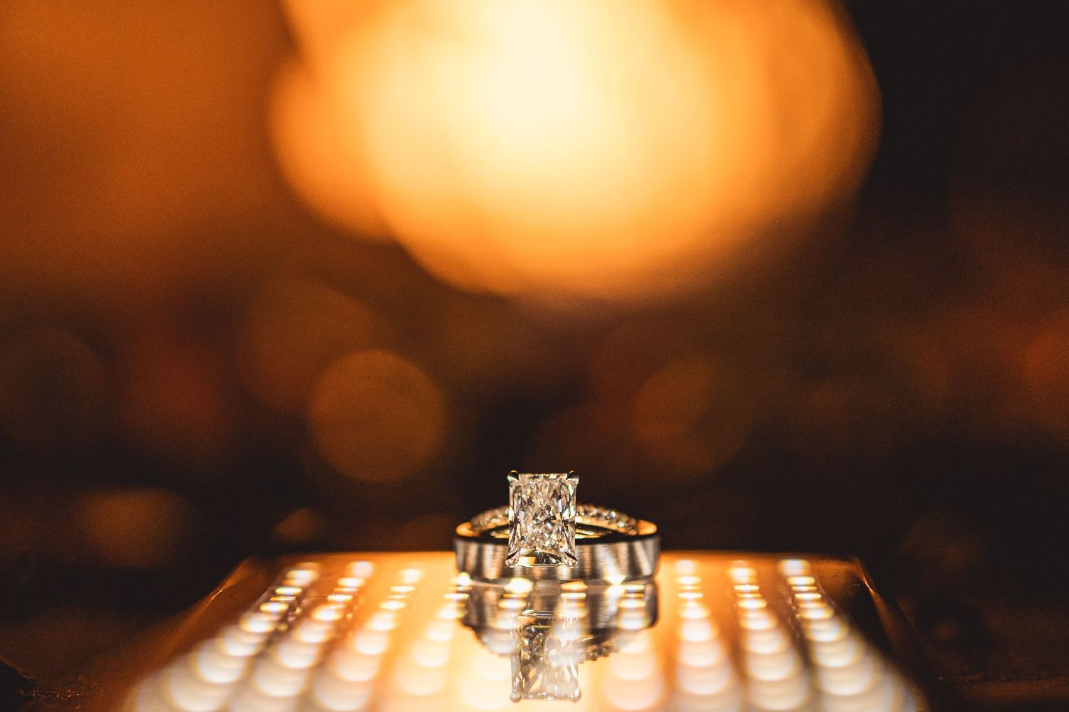 A sparkling diamond engagement ring captured with warm bokeh lighting in the background.