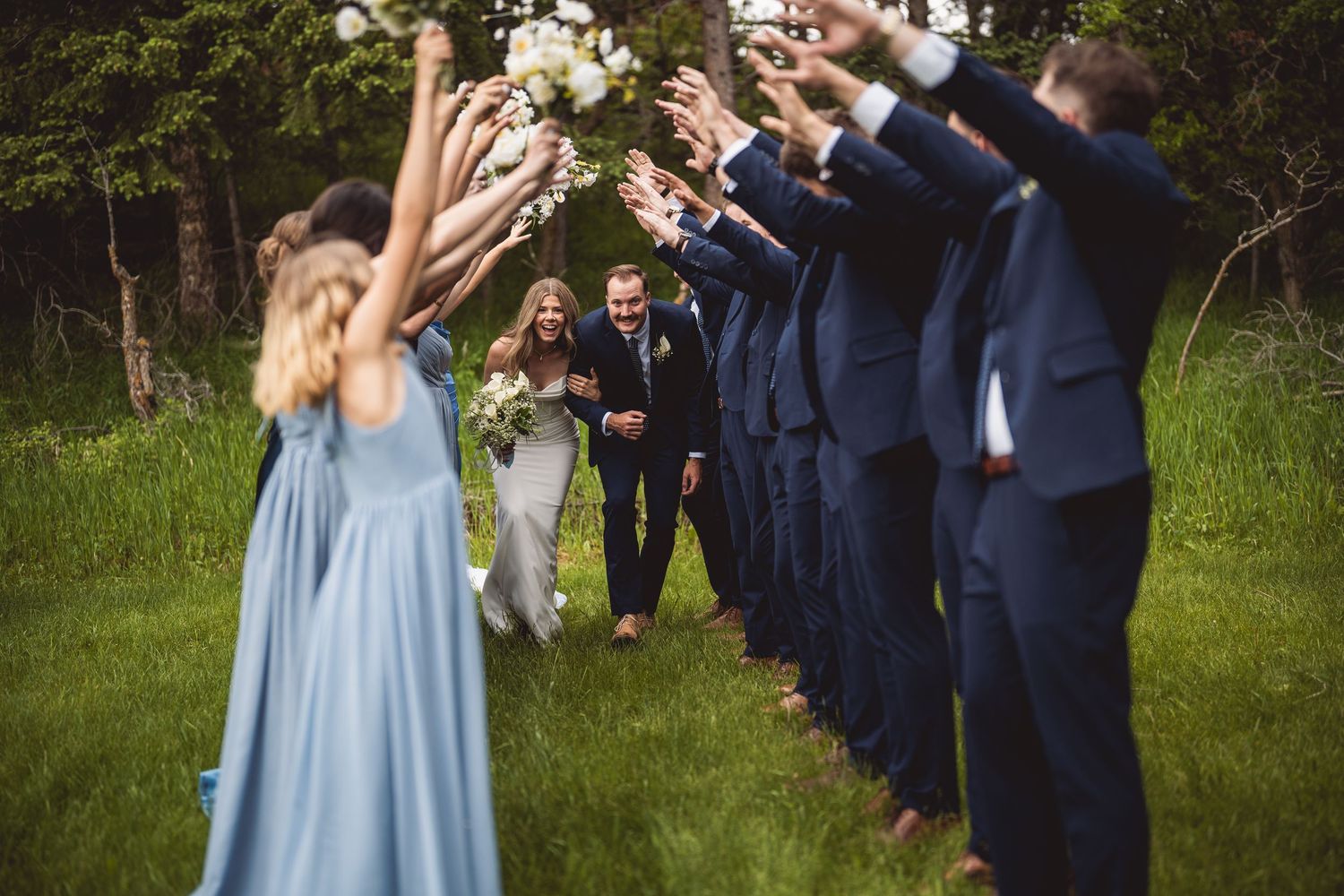 Wedding party celebrating outdoors with bridesmaids in blue dresses and groomsmen in navy suits.