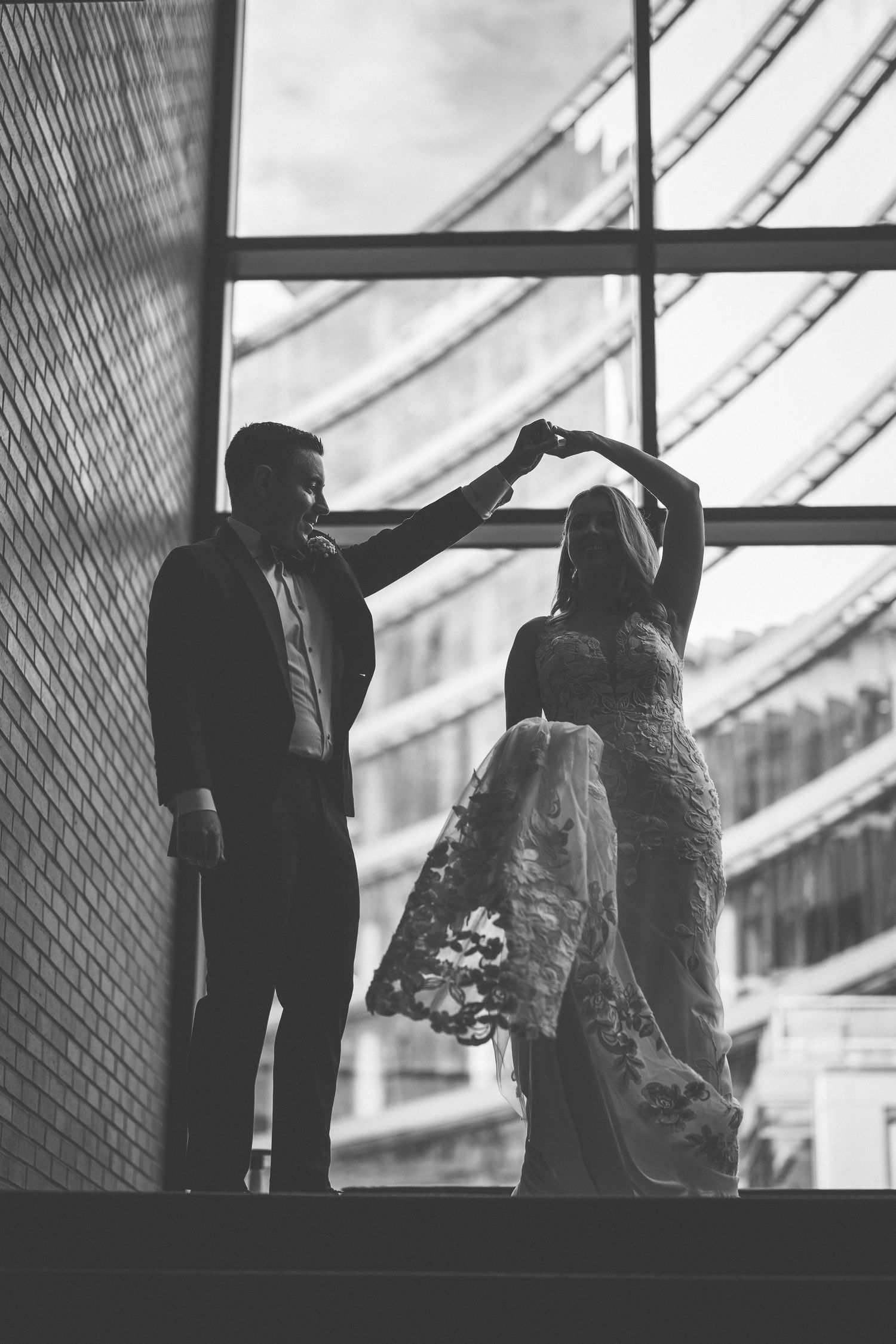 Artistic black and white silhouettes of a couple by large industrial windows.