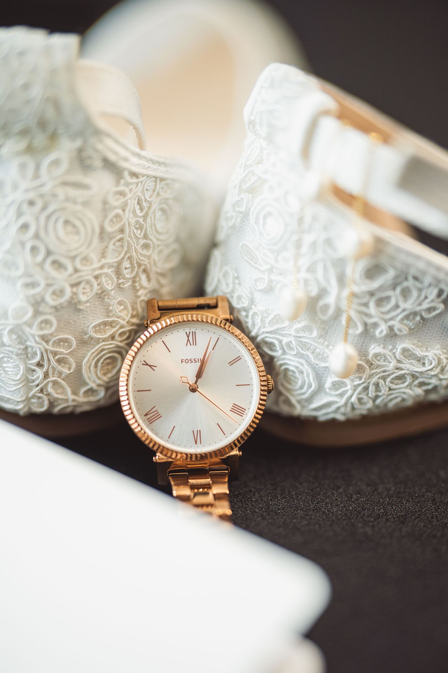 Elegant rose gold watch placed next to delicate lace wedding shoes.