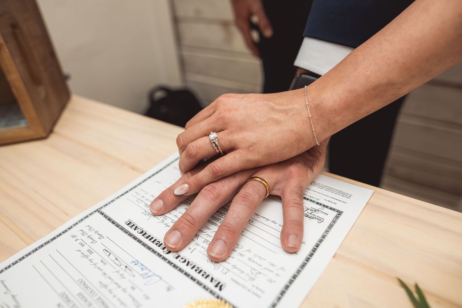 Hands signing paperwork on wooden desk with documents spread out.