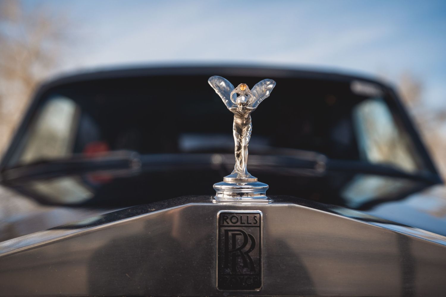 Close-up of the iconic Rolls-Royce Spirit of Ecstasy hood ornament on a luxury black vehicle.