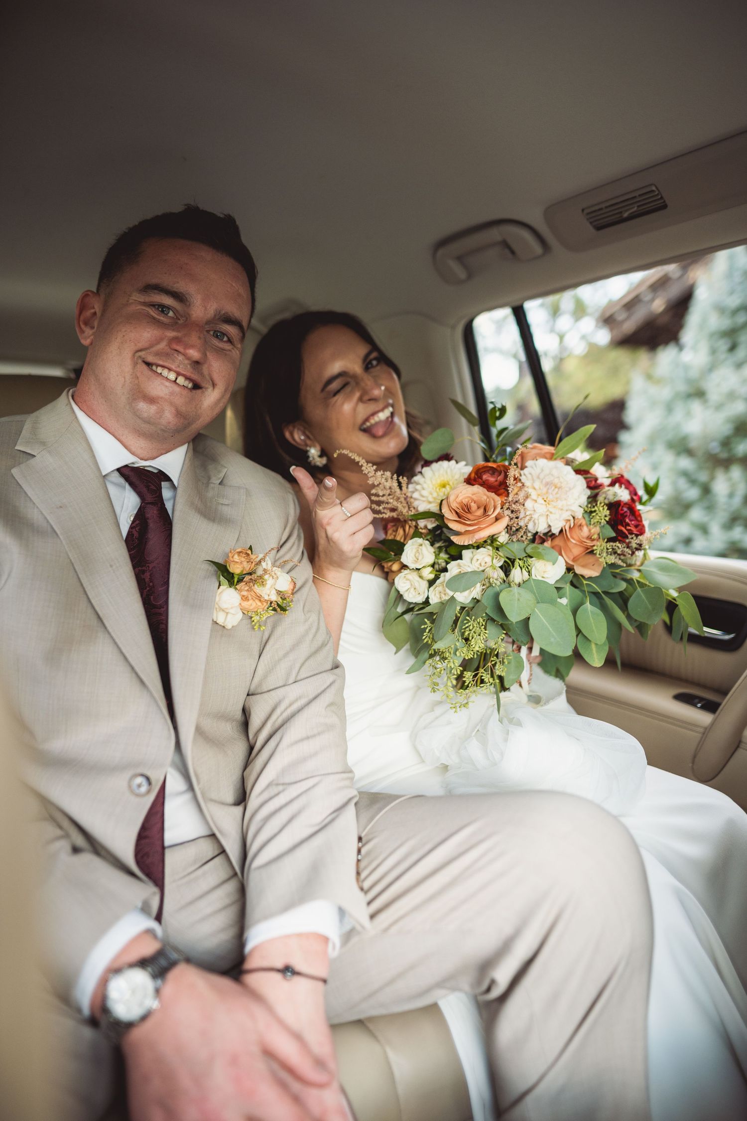 Wedding couple sharing joyful moment in back seat of vintage car with floral bouquet.