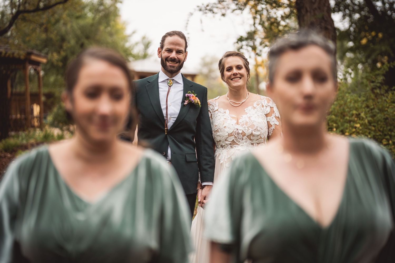Wedding party members in sage green dresses smile together outdoors.