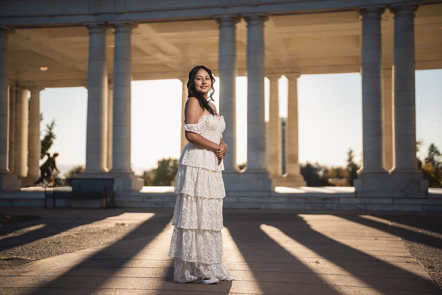 Classic portrait at golden hour featuring a tiered white dress among grand columns.