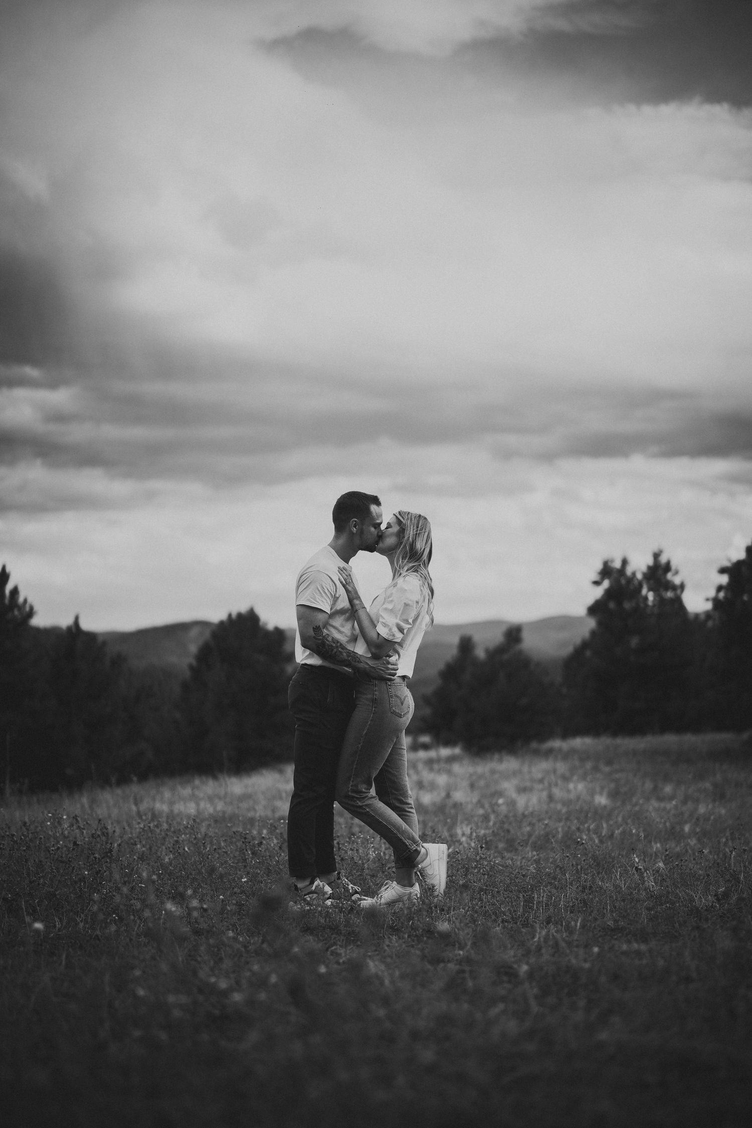 Romantic black and white photo of a couple in a meadow under cloudy skies.