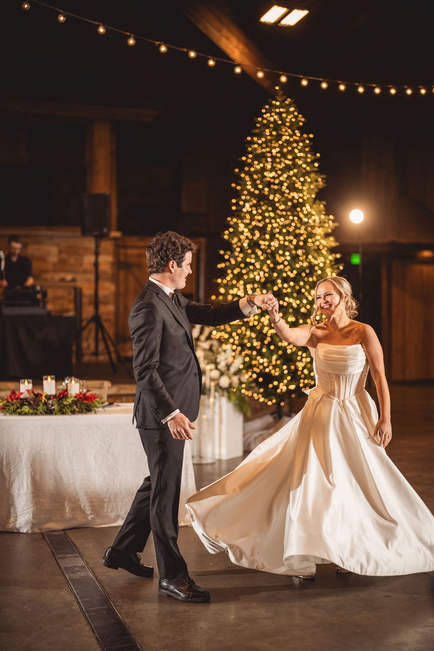 Bride and groom share first dance in front of a glowing Christmas tree at elegant winter wedding reception.