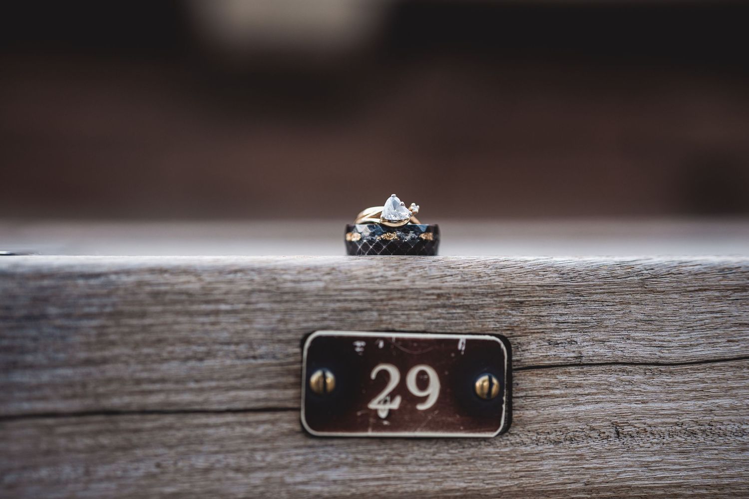 Two rings displayed on a wooden surface next to a vintage number 29 plaque, featuring a diamond engagement ring.