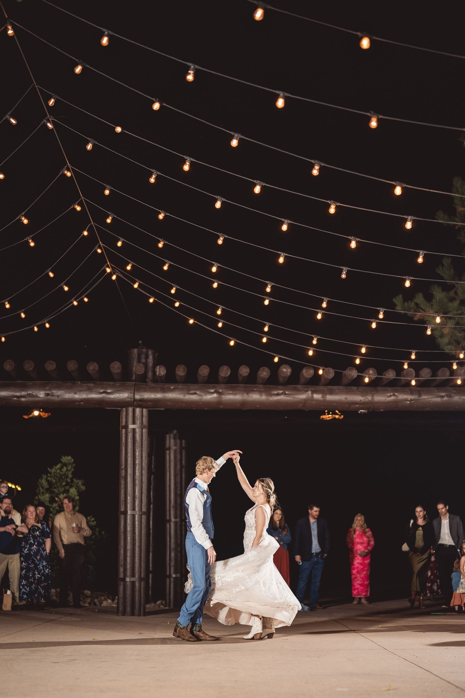 Bride and groom share first dance under string lights at outdoor wedding reception at night.