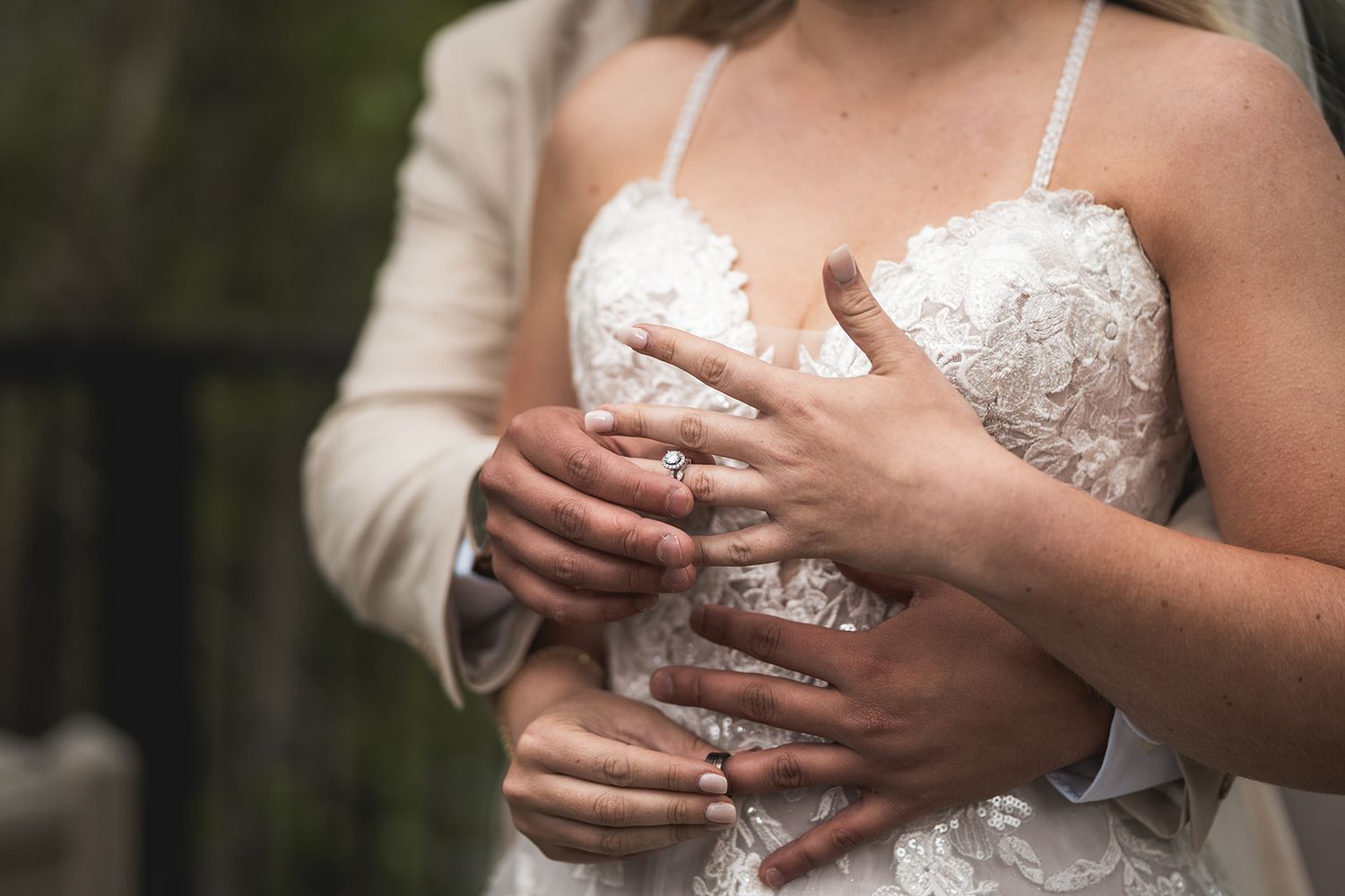 Bride and groom holding hands showing wedding rings, bride wearing lace wedding dress.