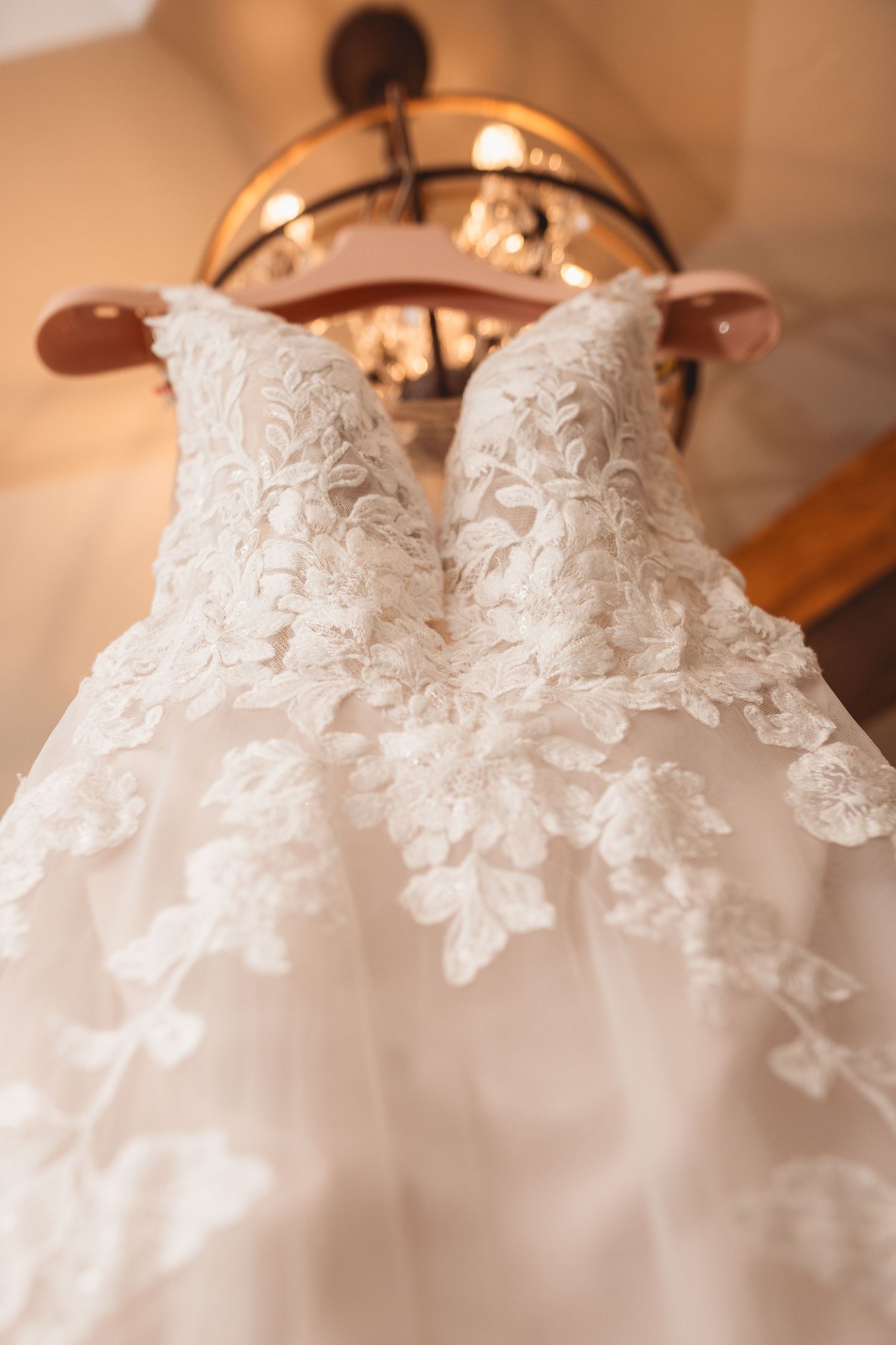 Detailed lace pattern on white wedding dress bodice with chandelier in background.
