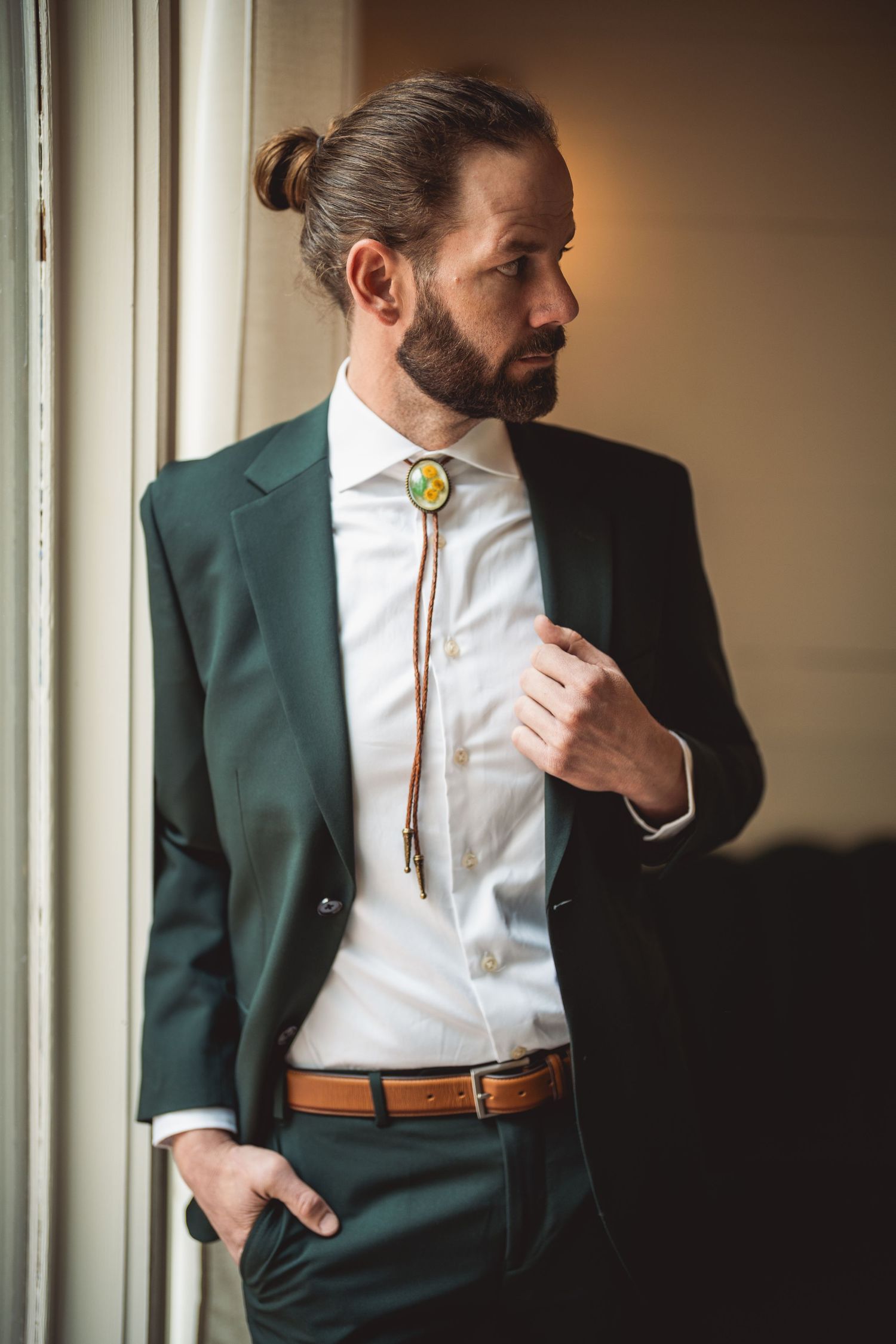 Stylish groom in dark green suit jacket and white shirt adjusting his tie.