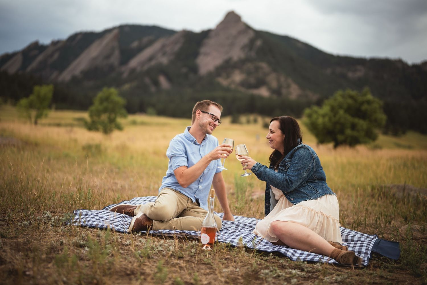A romantic picnic scene with mountain views and a checkered blanket spread on golden grass.