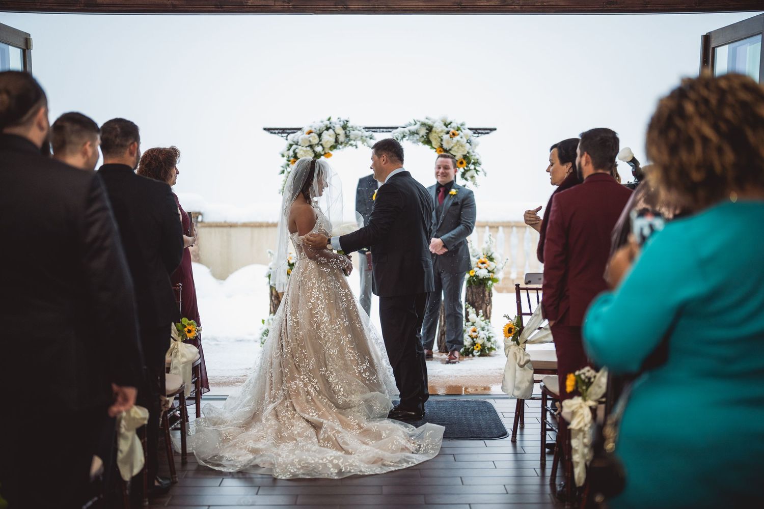 Wedding ceremony in a bright venue with guests seated facing a floral arch.