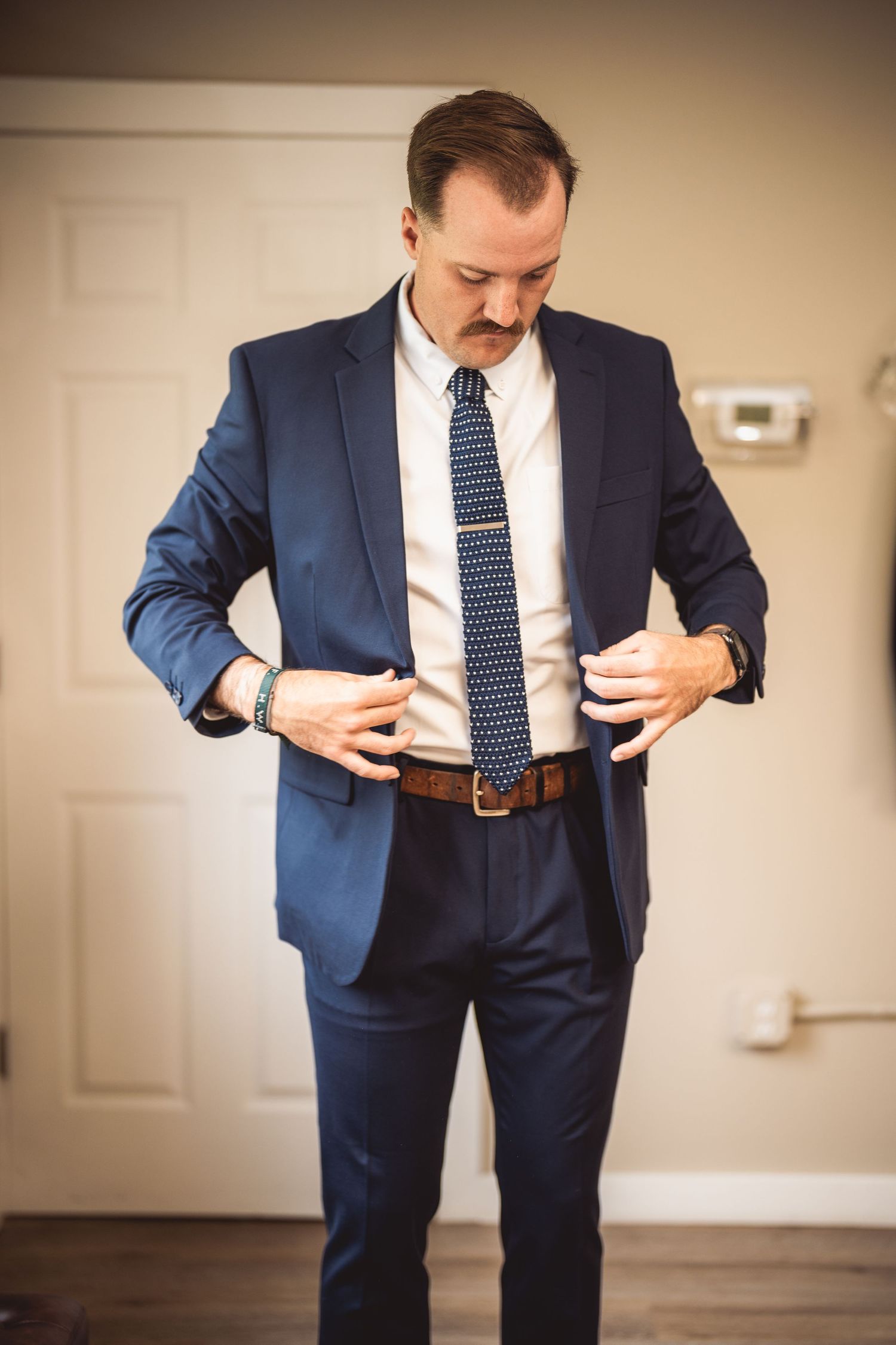 Man in navy suit adjusts his clothing while preparing for formal event.