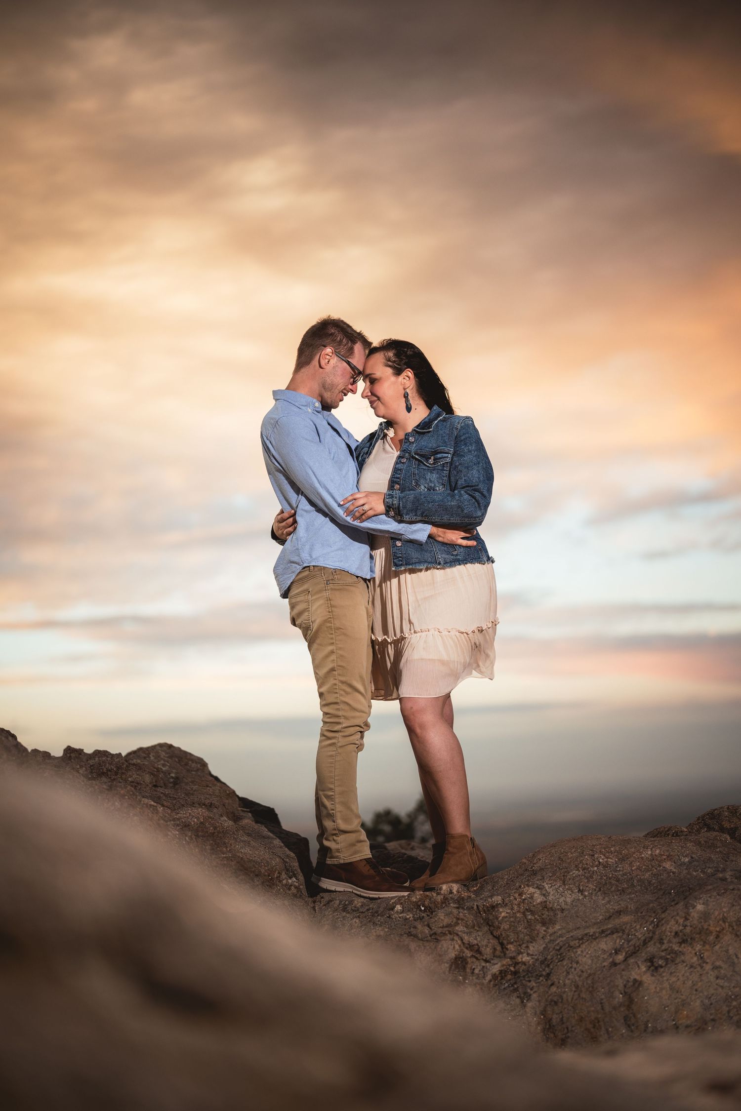An intimate moment captured against a dramatic sunset sky with mountains in the background.