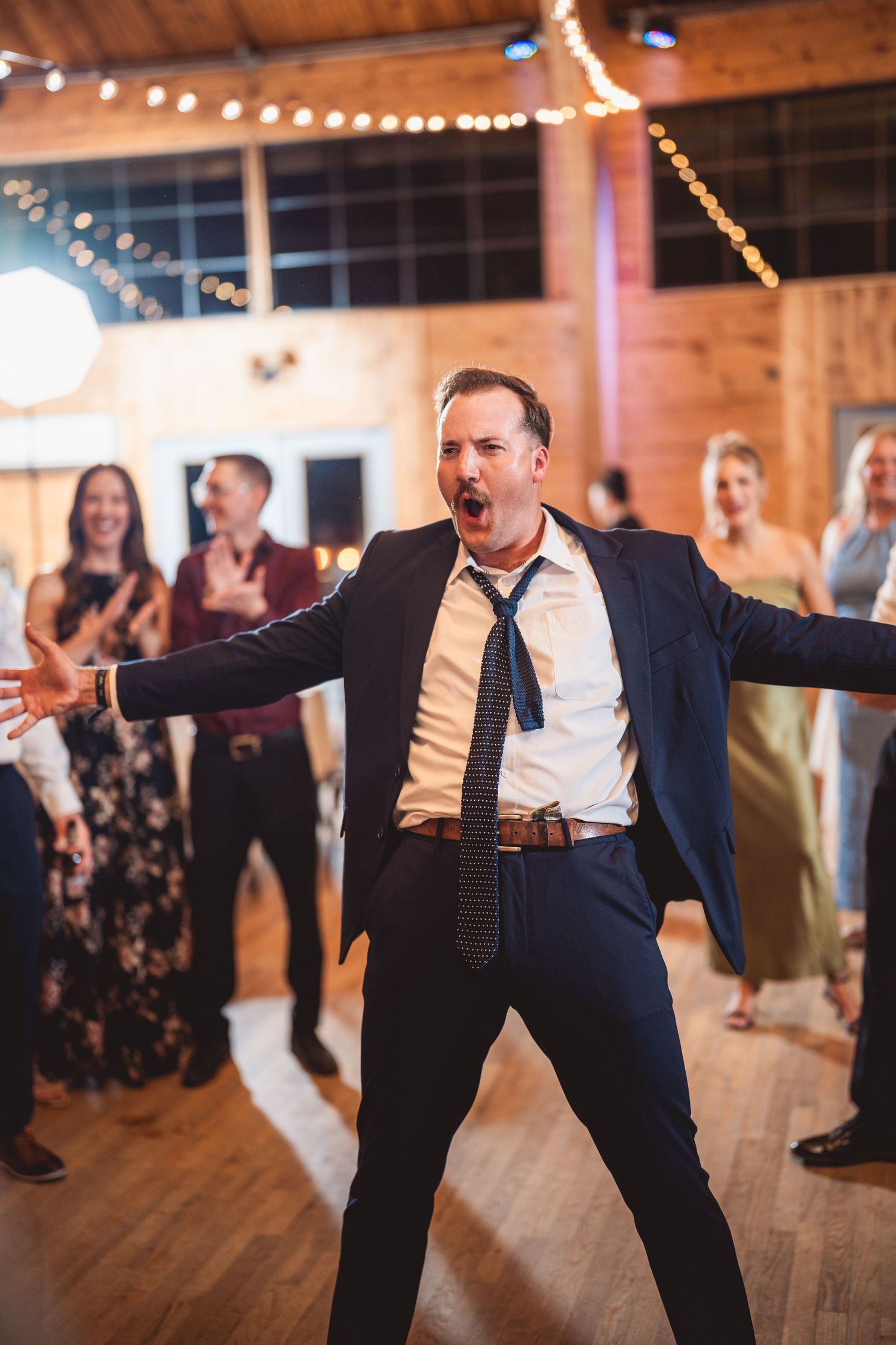 Guests dancing energetically on a wooden dance floor under warm lighting.