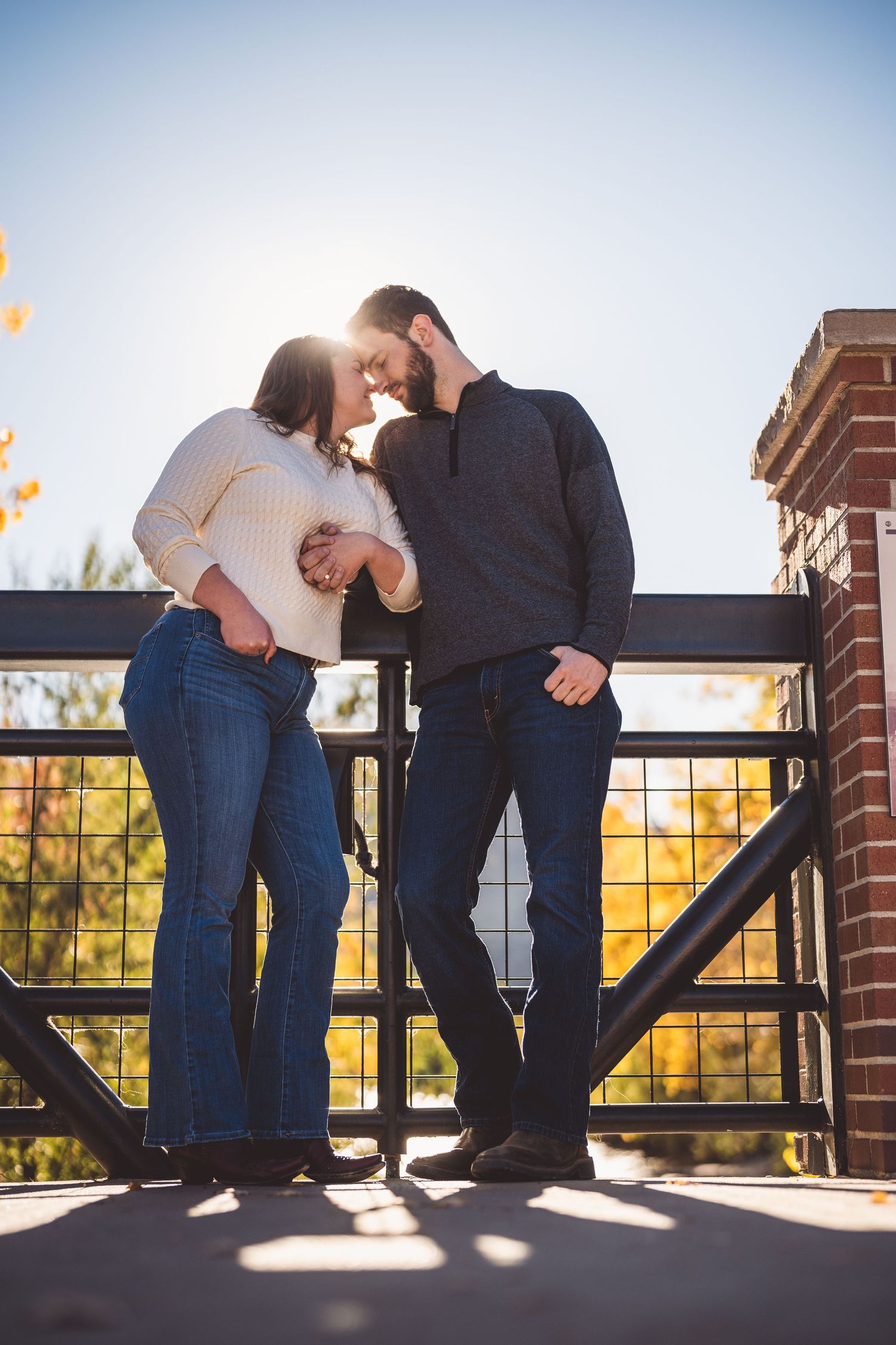 Silhouetted couple sharing a romantic moment against a brick railing during sunset.