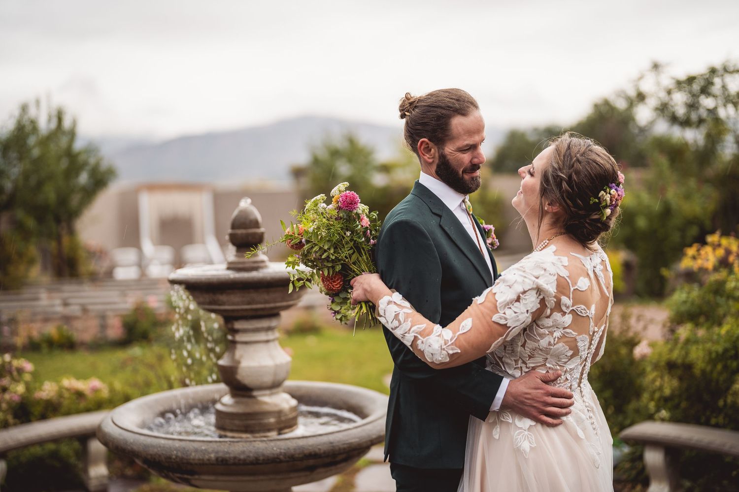 A romantic wedding couple embraces on a terrace with mountain views in the background.