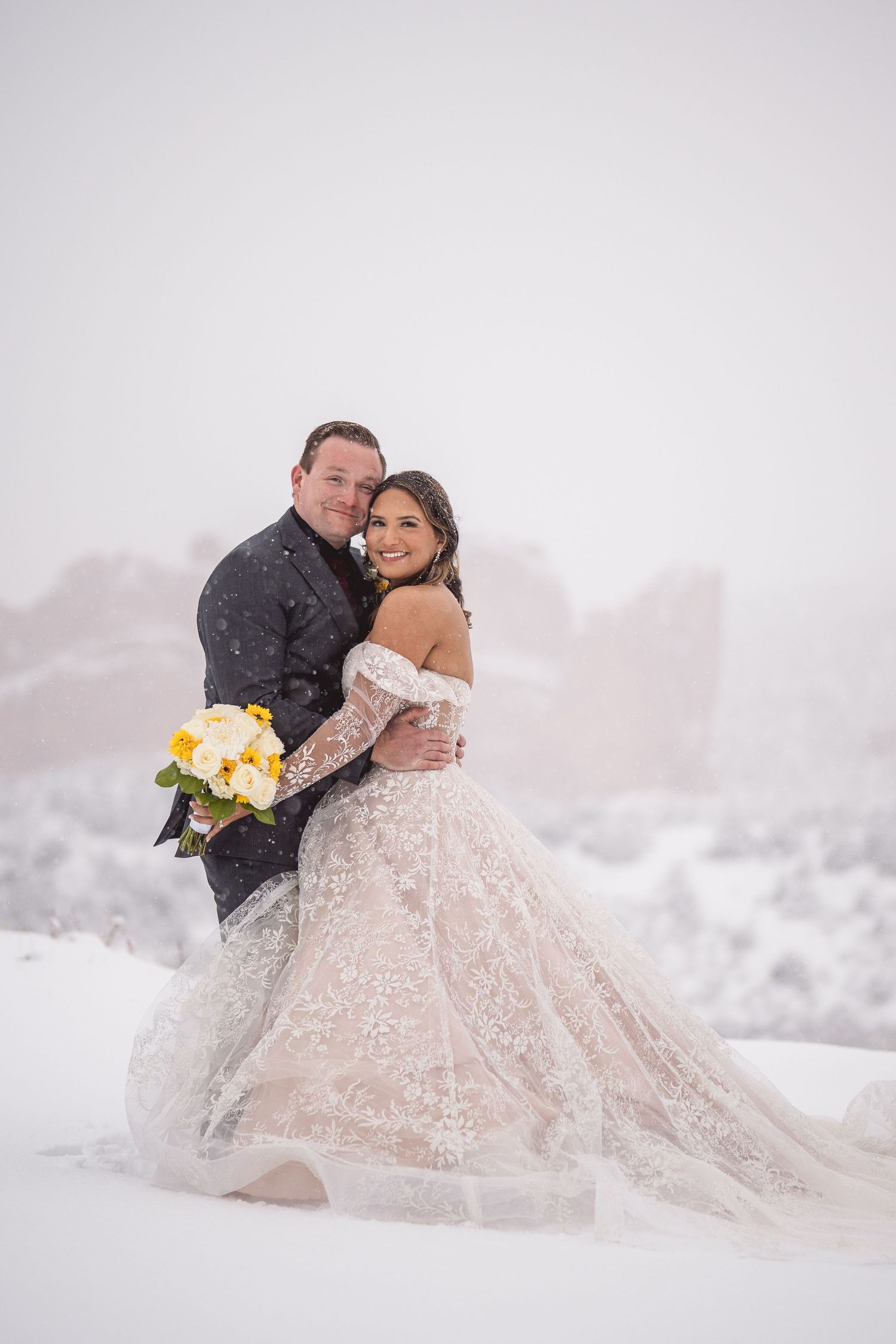 Couple in wedding attire embracing in dreamy snow-covered mountain setting.