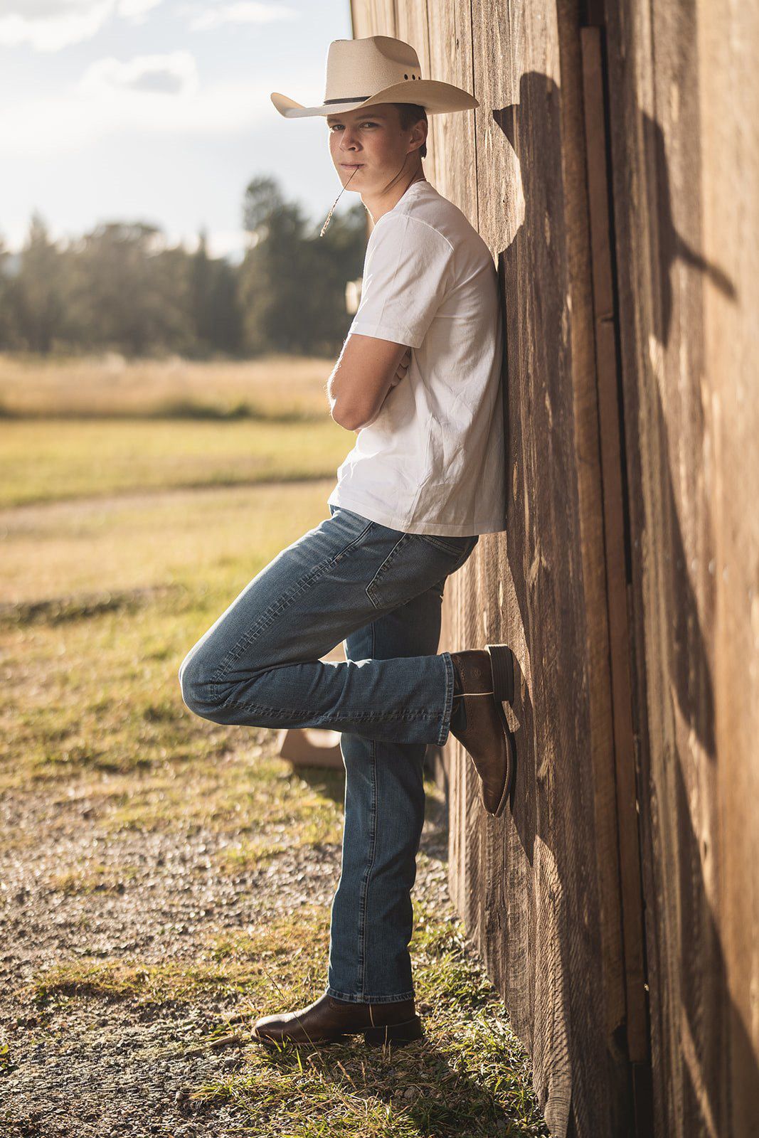 Figure in western wear leaning against wooden post in rustic outdoor setting.