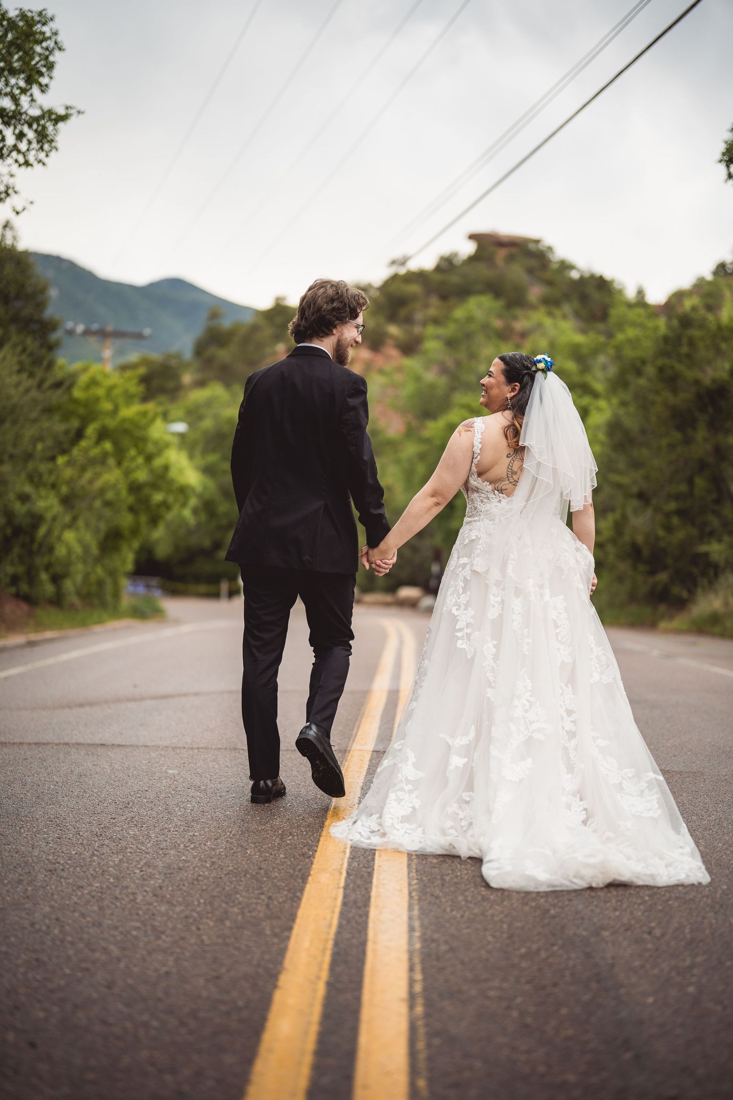 Wedding couple walks together down a mountain road with dramatic dress train following behind.