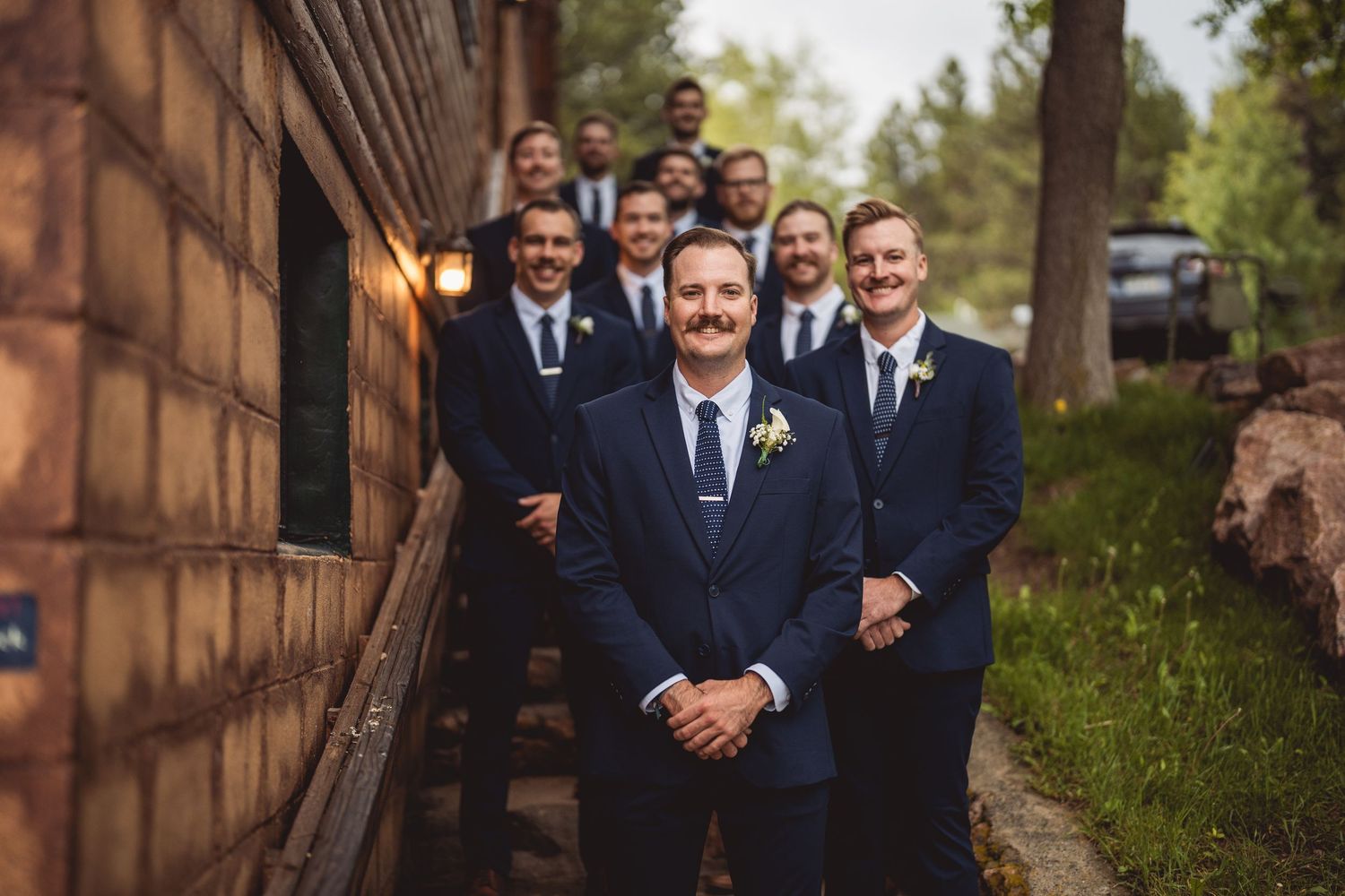 Wedding party poses together on rustic pathway surrounded by autumn foliage.