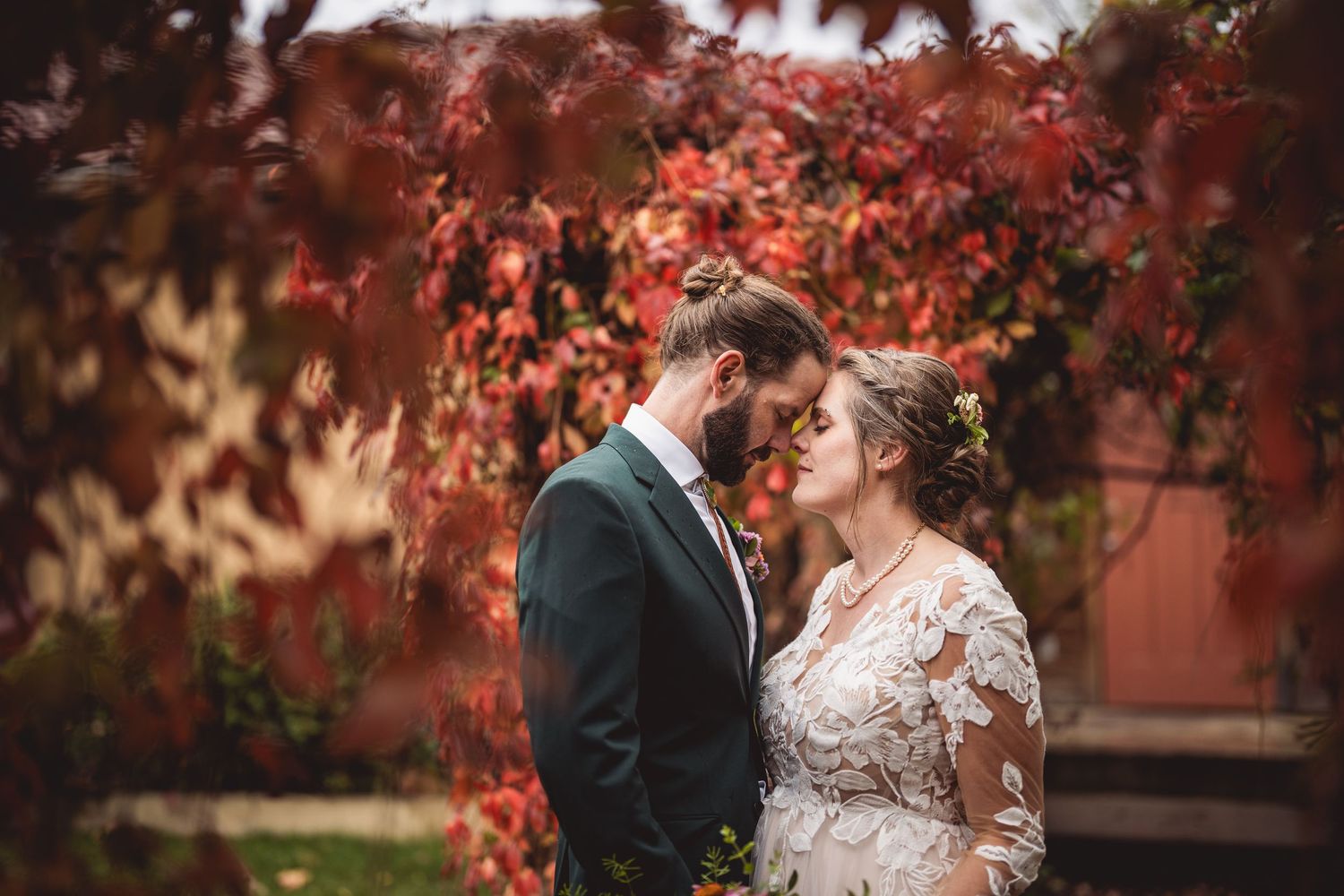 A romantic wedding photo with vibrant red autumn foliage in the background.