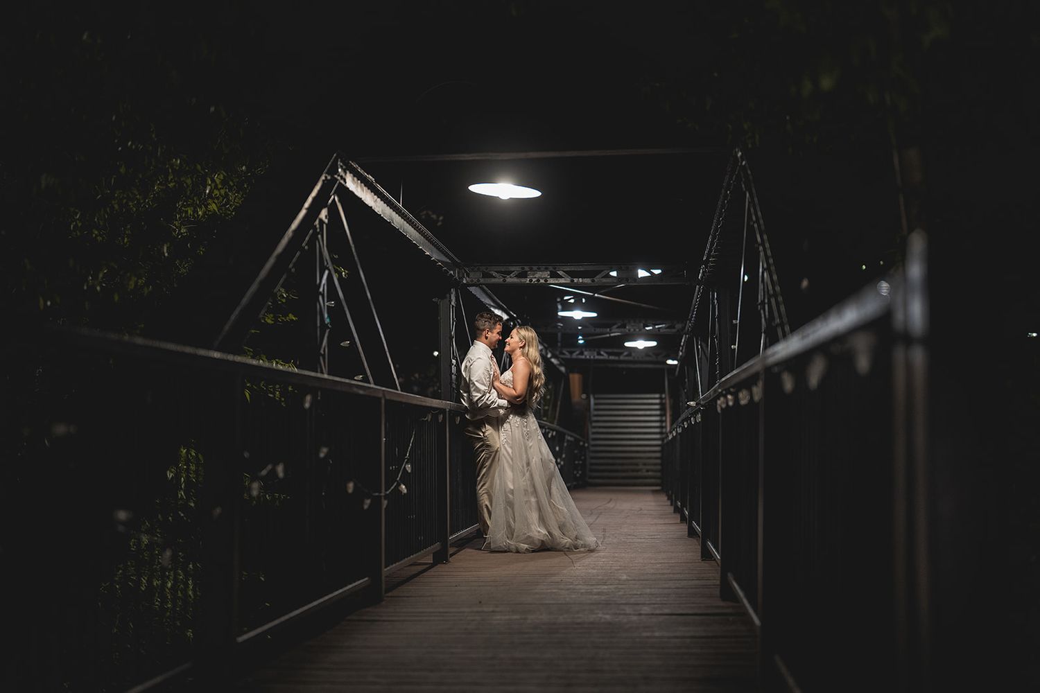 Couple embraces on a dimly lit bridge at night in a romantic wedding portrait.
