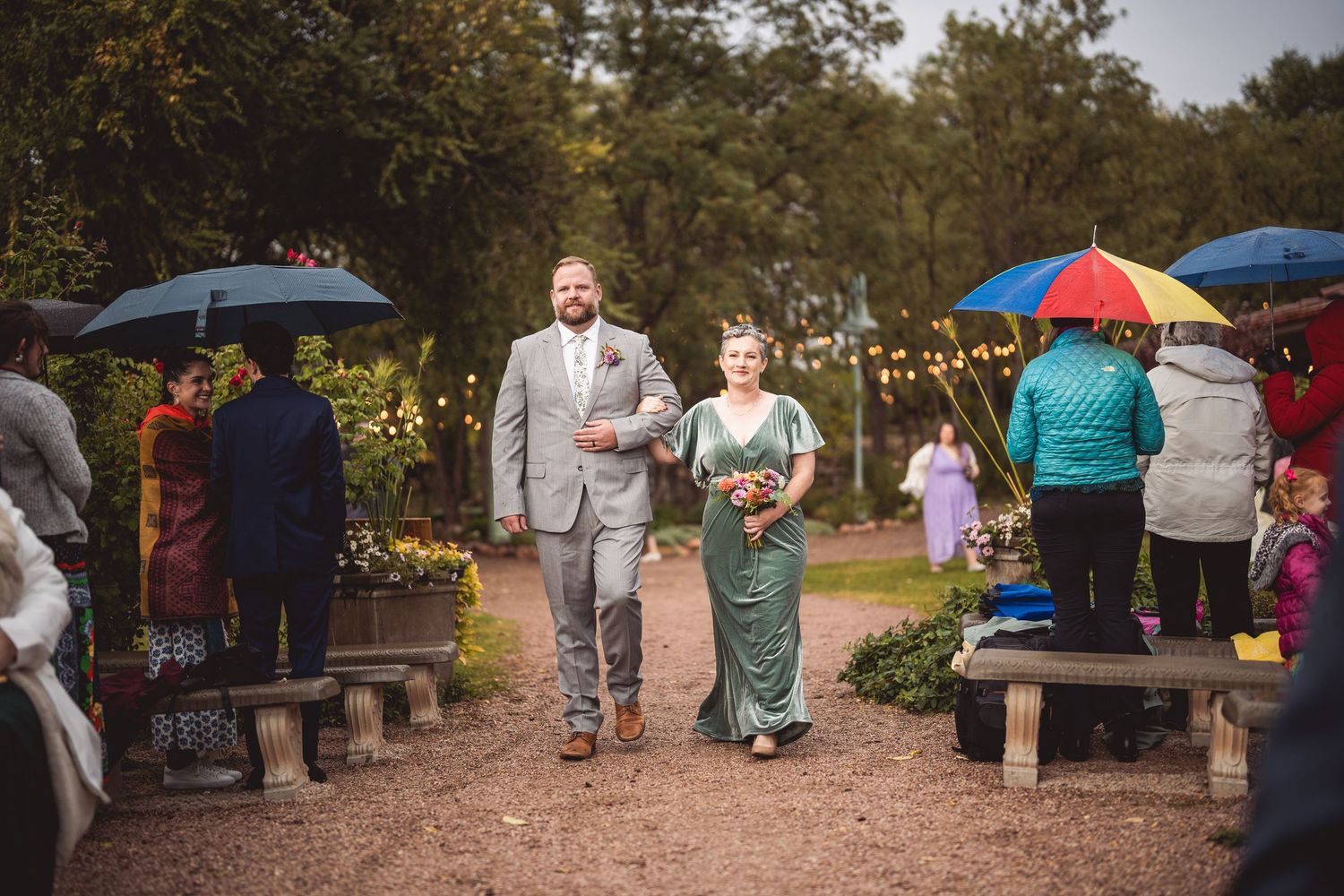 Wedding ceremony setup on a gravel path with colorful umbrellas and string lights.