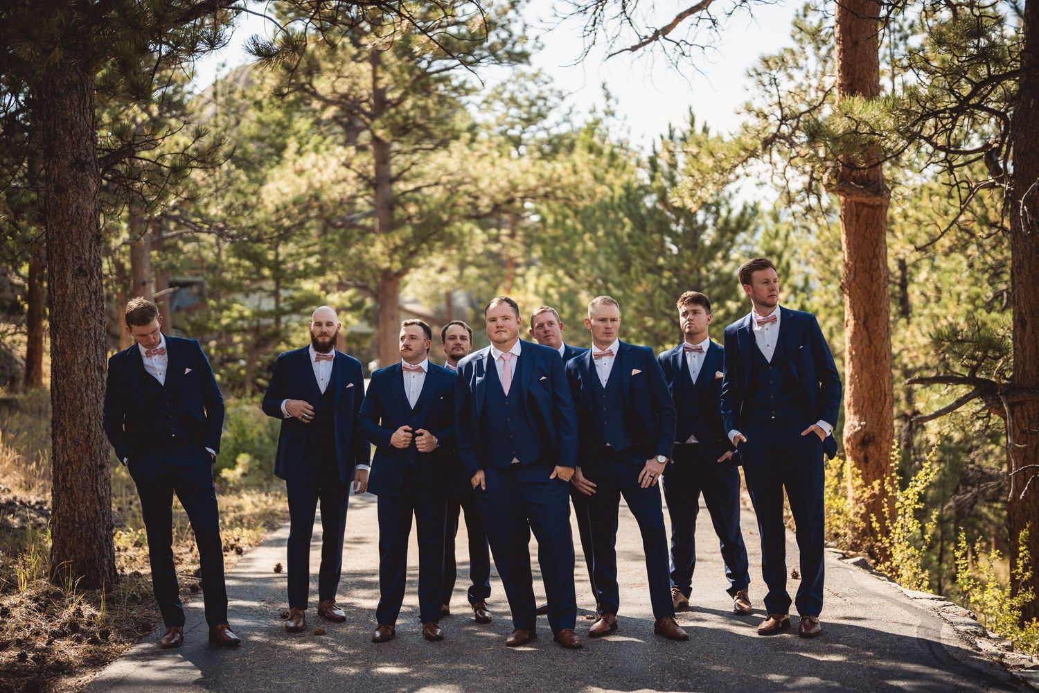 Wedding party members pose casually together on a sunlit mountain path.