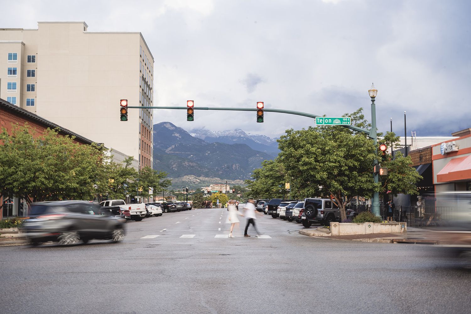Urban street intersection with traffic lights and buildings against a mountain backdrop.