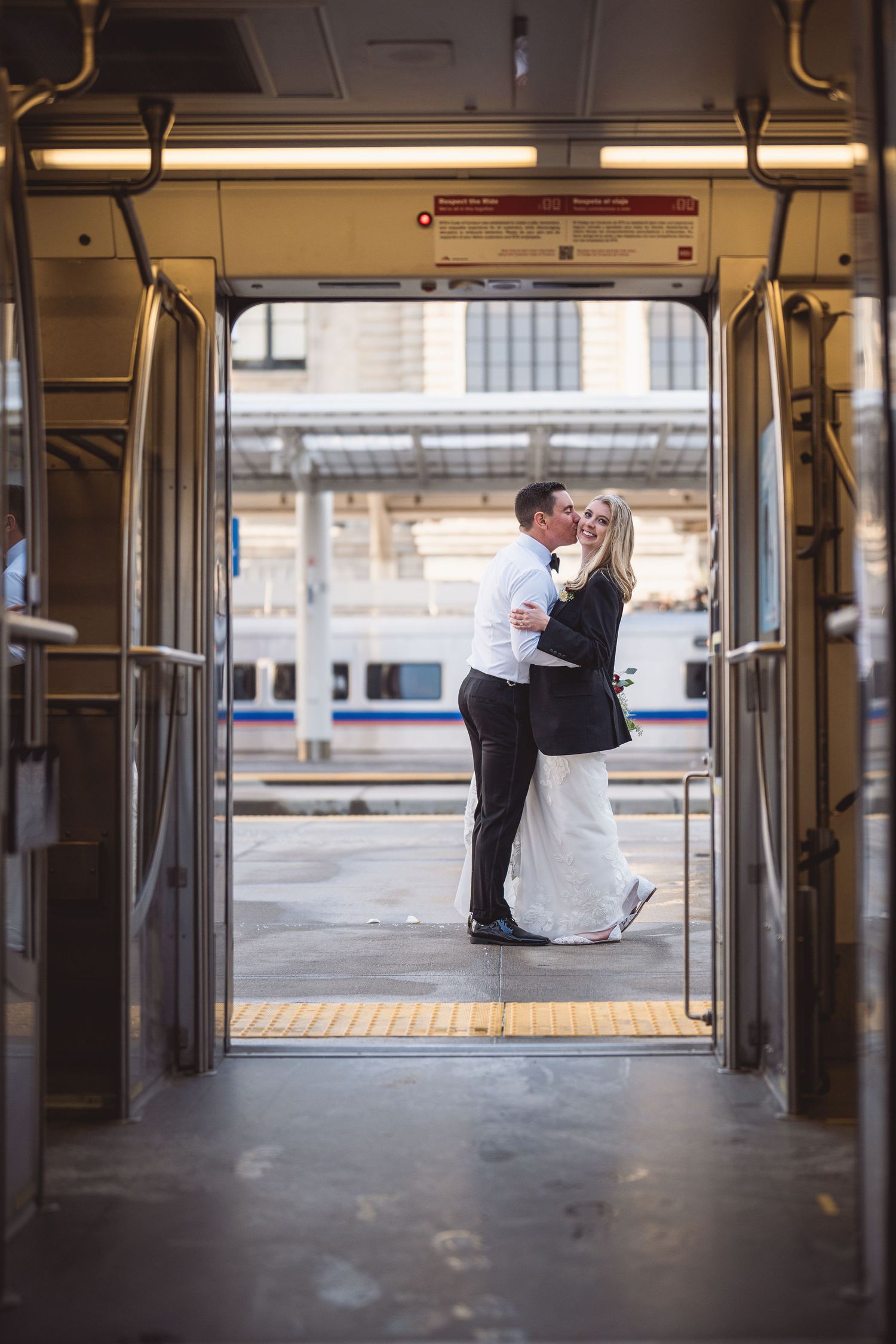 Bride and groom kissing in train doorway at station, wedding portrait with white dress and black suit.