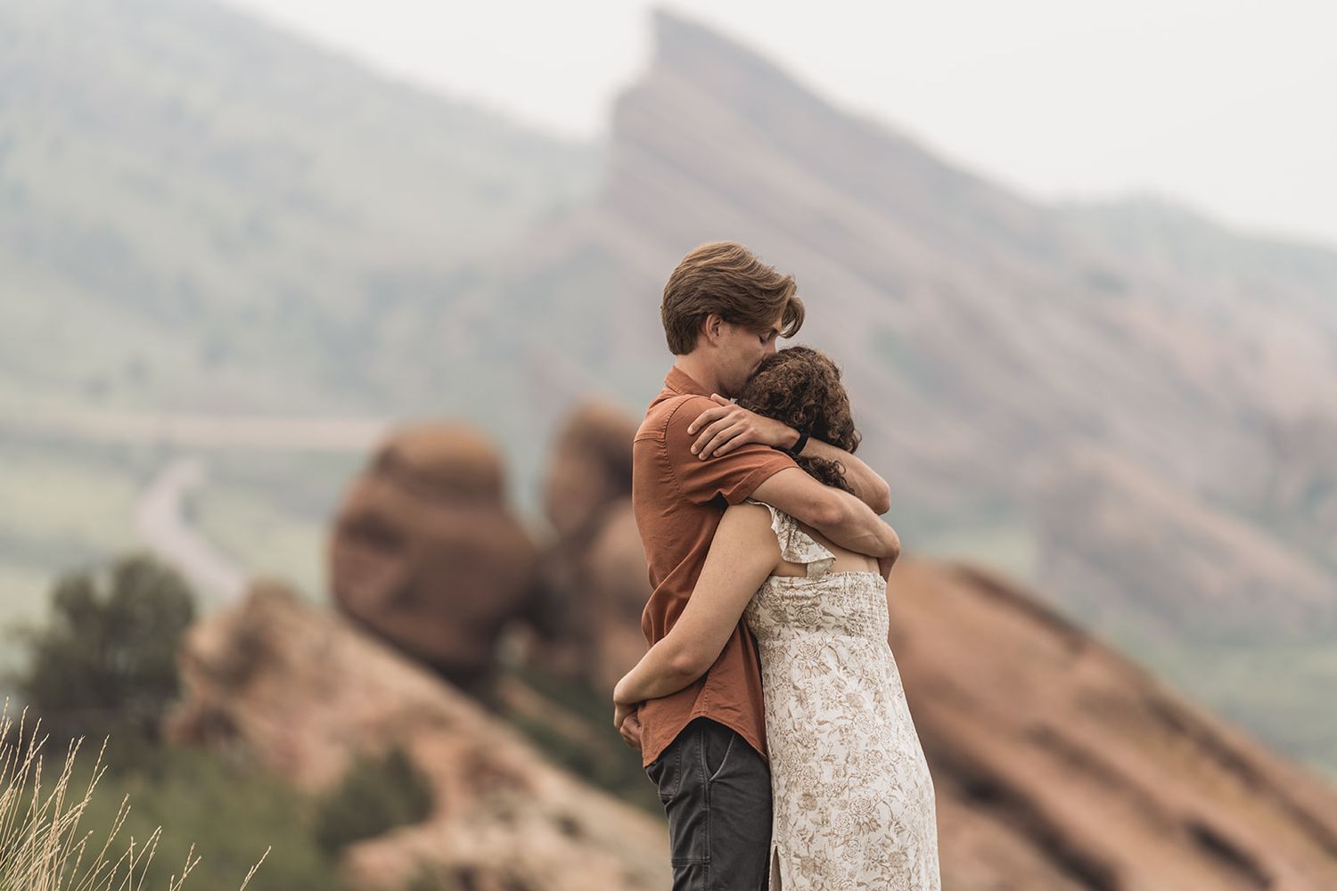 Romantic couple embracing tenderly with stunning red rock formations and misty mountains behind them.