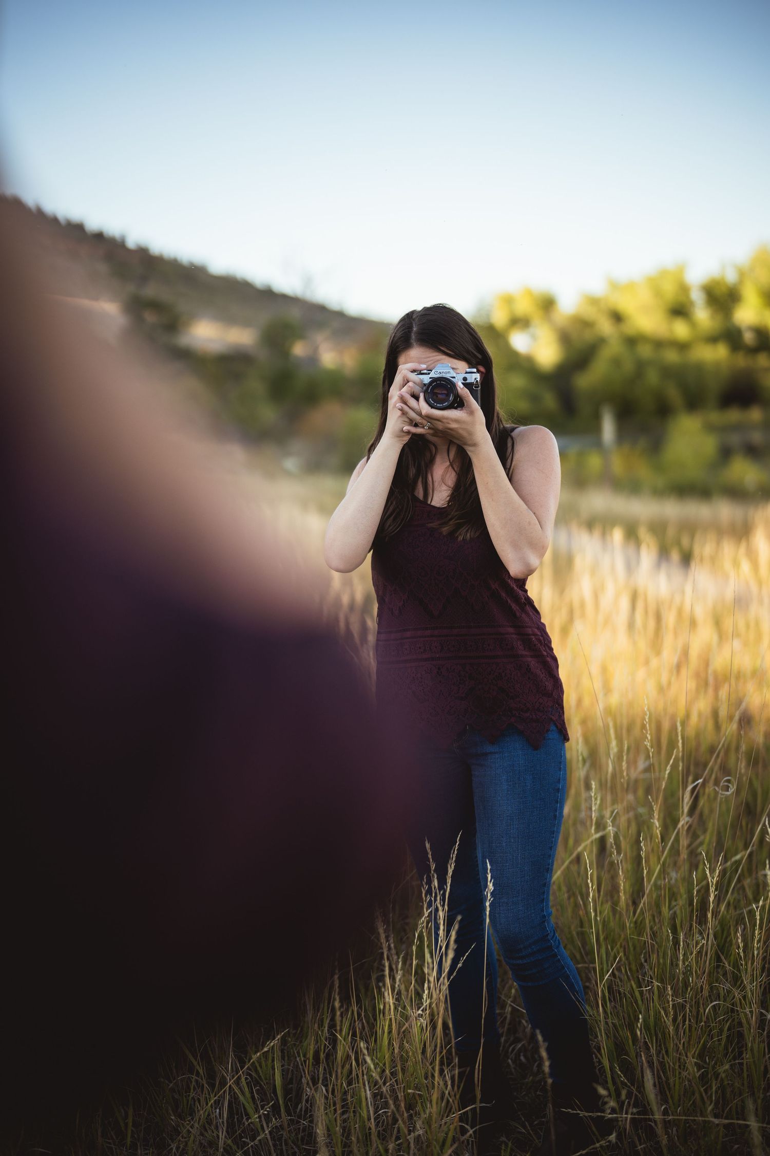 Person with a camera stands in a field of tall grass during golden hour.