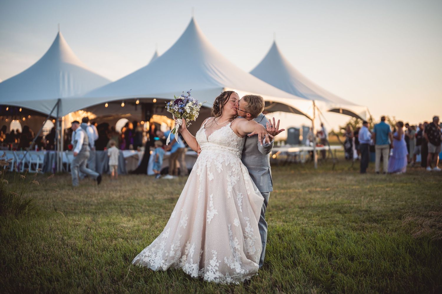 Couple shares intimate moment outside wedding reception tent at sunset.