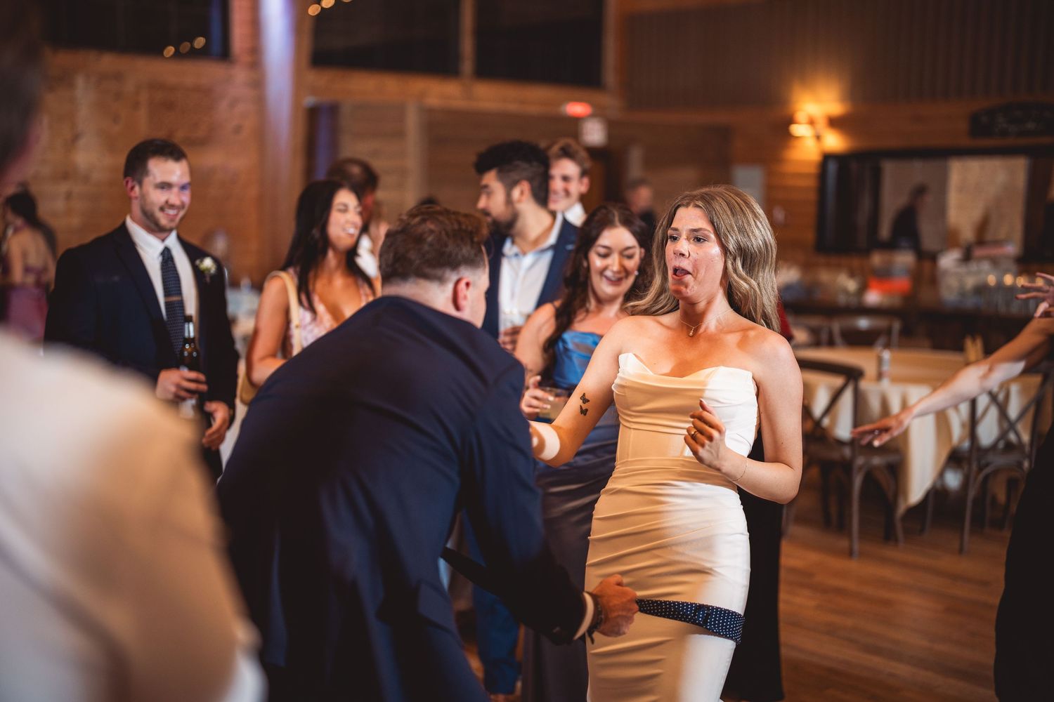 Wedding reception with guests dancing in a rustic venue with warm lighting.