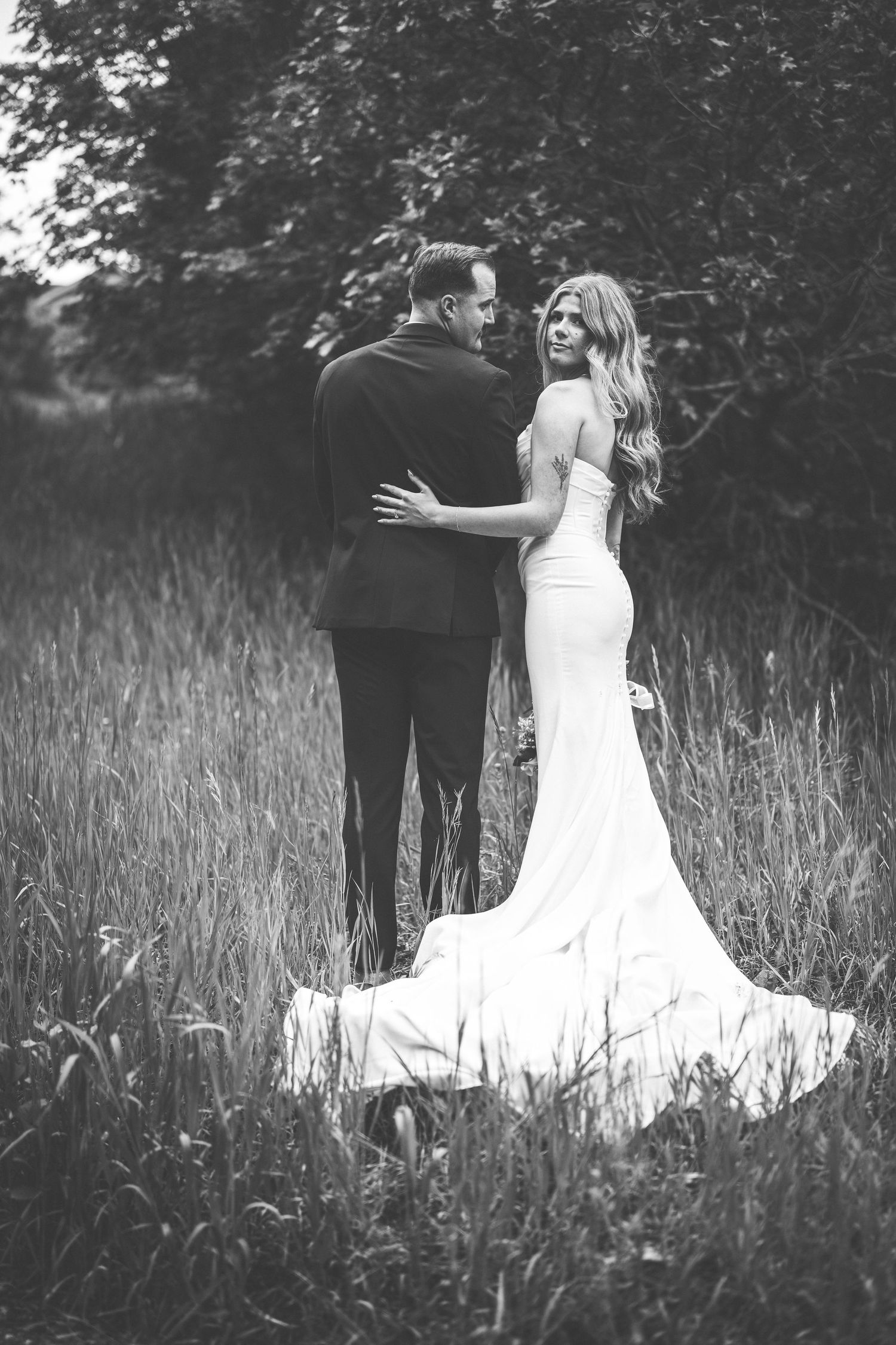 Black and white wedding portraits showing couple walking through tall grass meadow.