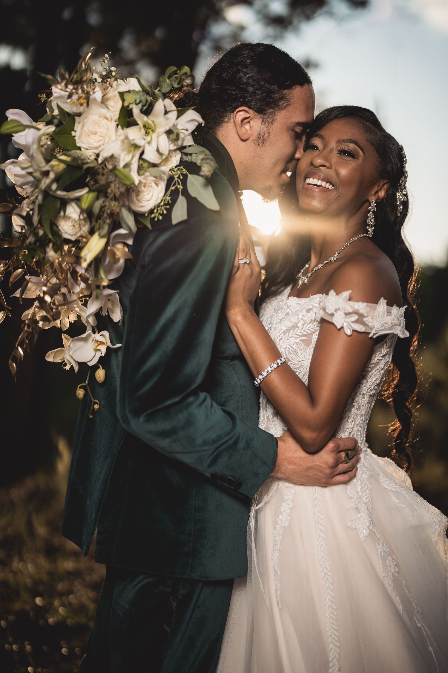 Candid wedding moment with elegant white dress and dark green suit at golden hour.