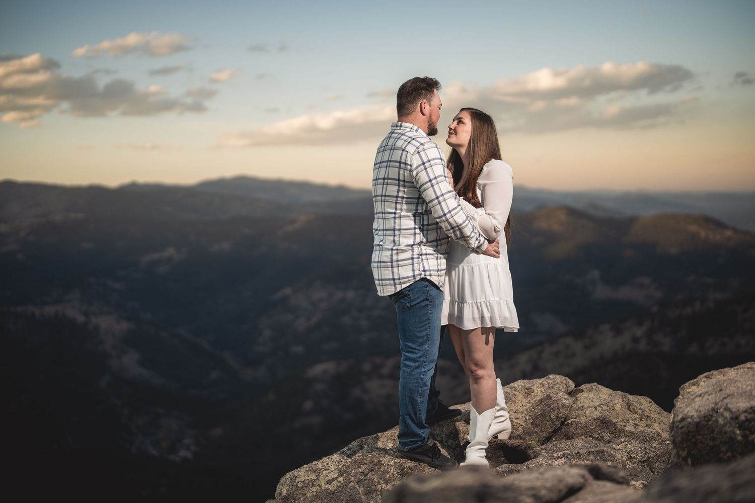 Couple embraces on mountain overlook during golden hour with panoramic valley views.