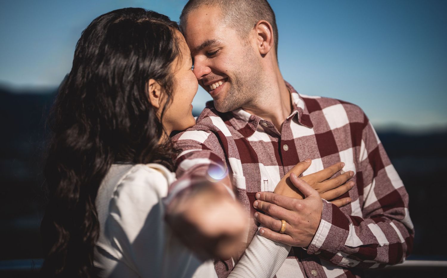 Couple embracing during outdoor photo session with blue sky background.