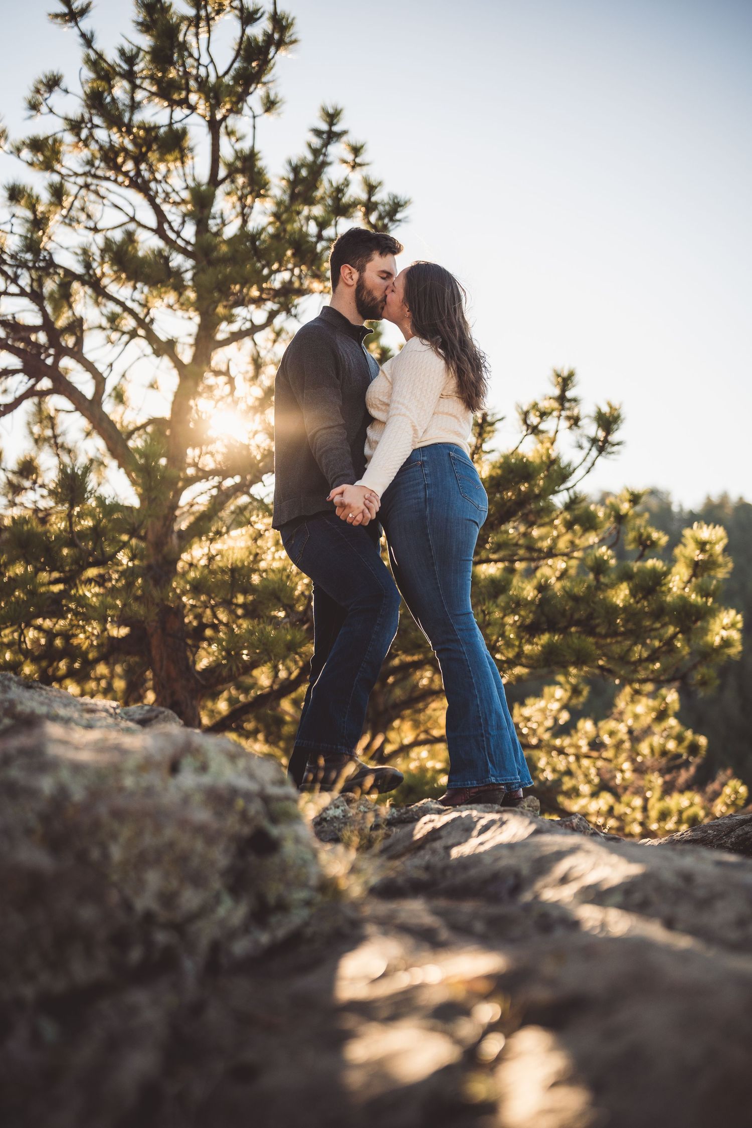 A romantic moment shared between two people standing on rocky terrain at golden hour.
