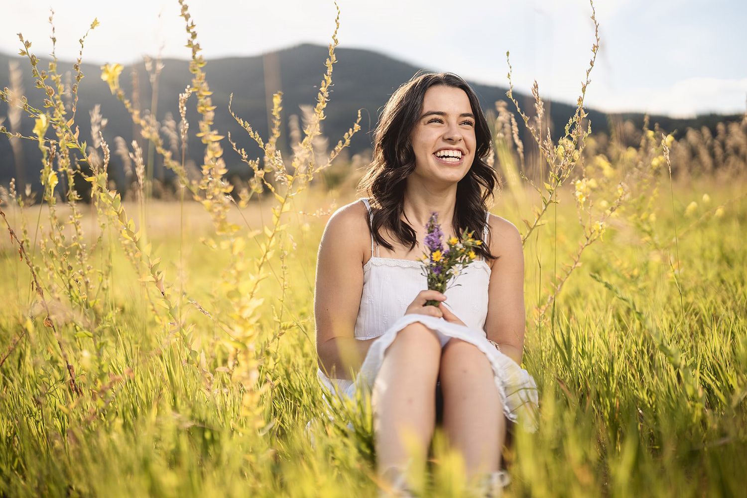 Candid portrait of woman laughing in a summer meadow with mountains in background.