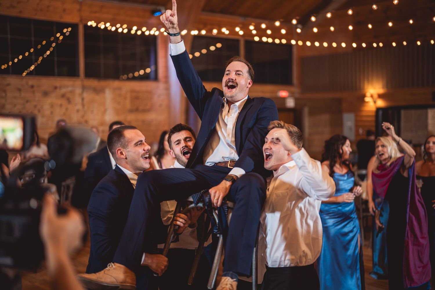 Lively wedding reception dance party with guests celebrating under warm string lights.