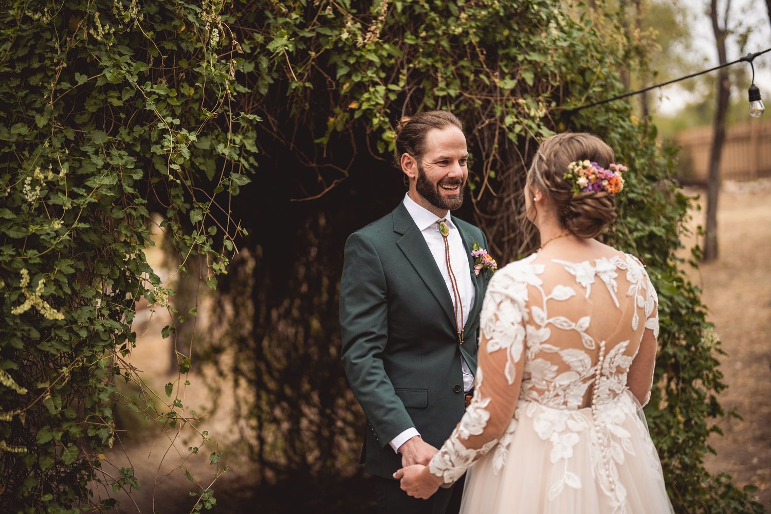 Newlyweds share loving moments during outdoor wedding photoshoot among trees.