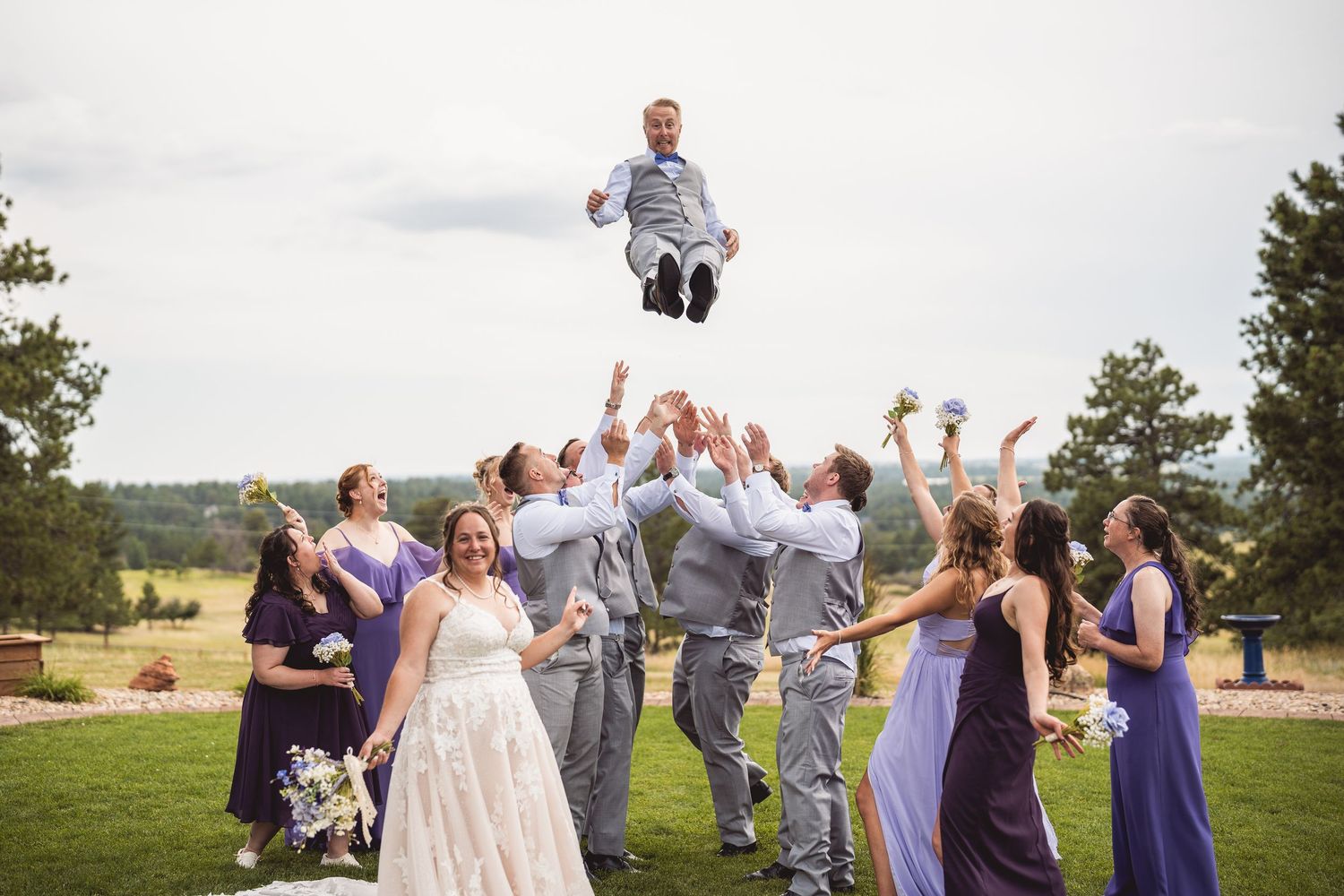 Joyful wedding party celebrating with energetic jumping poses against a scenic outdoor backdrop.