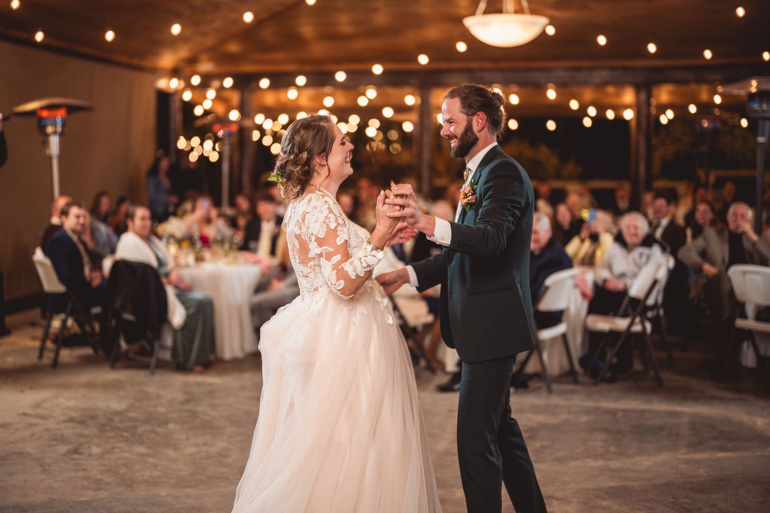A romantic first dance unfolds beneath glowing string lights in a spacious wedding venue.