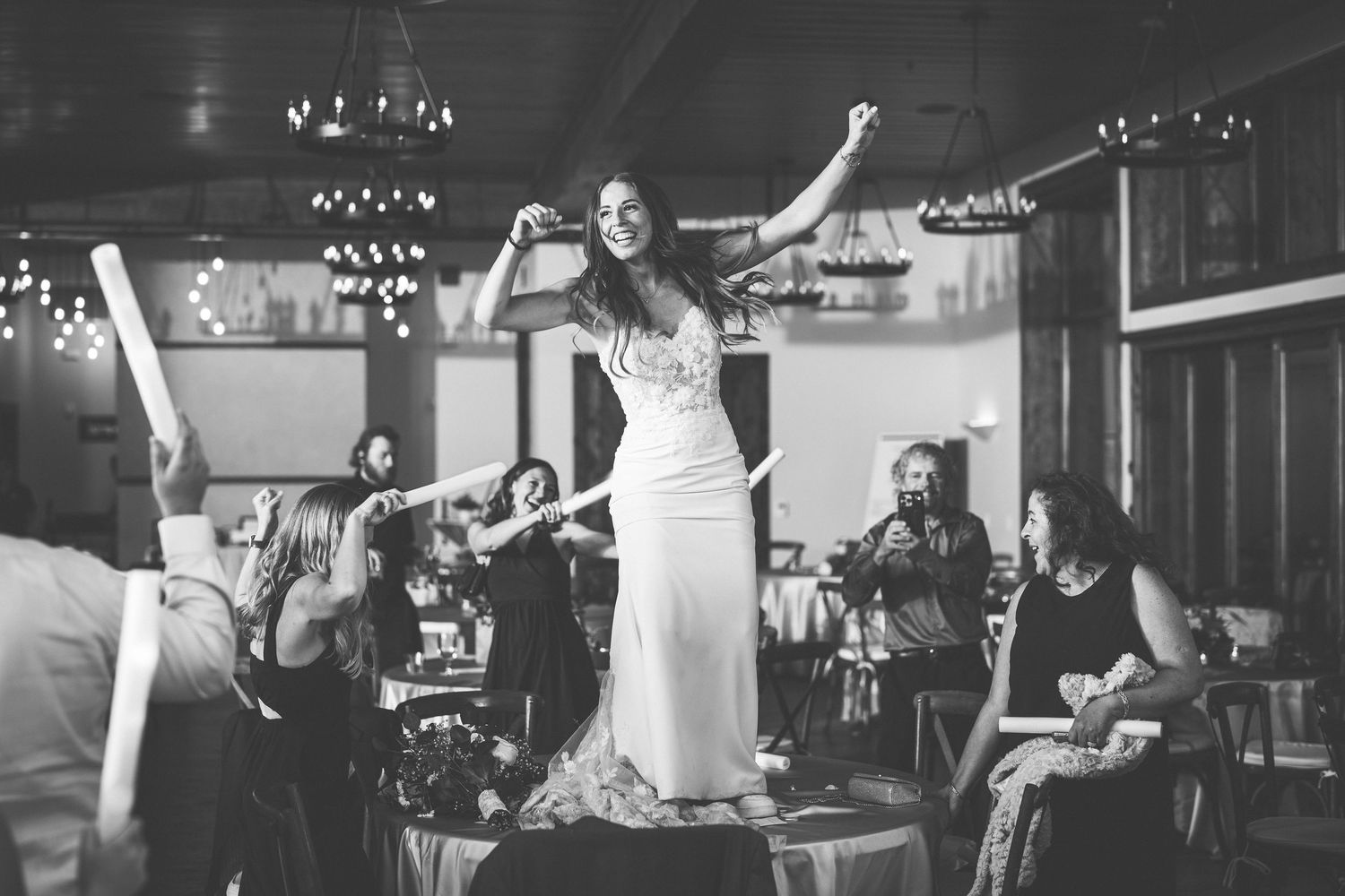 Black and white photo of a bride dancing joyfully at her wedding reception surrounded by guests.