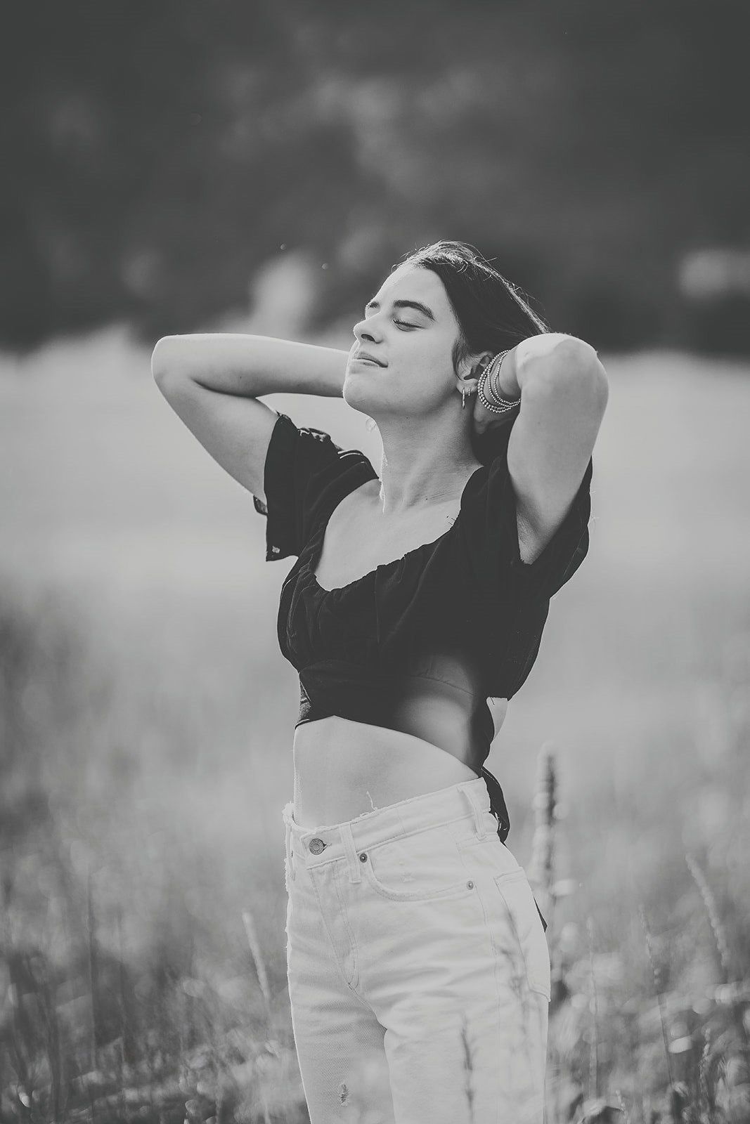 Black and white portrait of woman with hands in hair standing in open field.