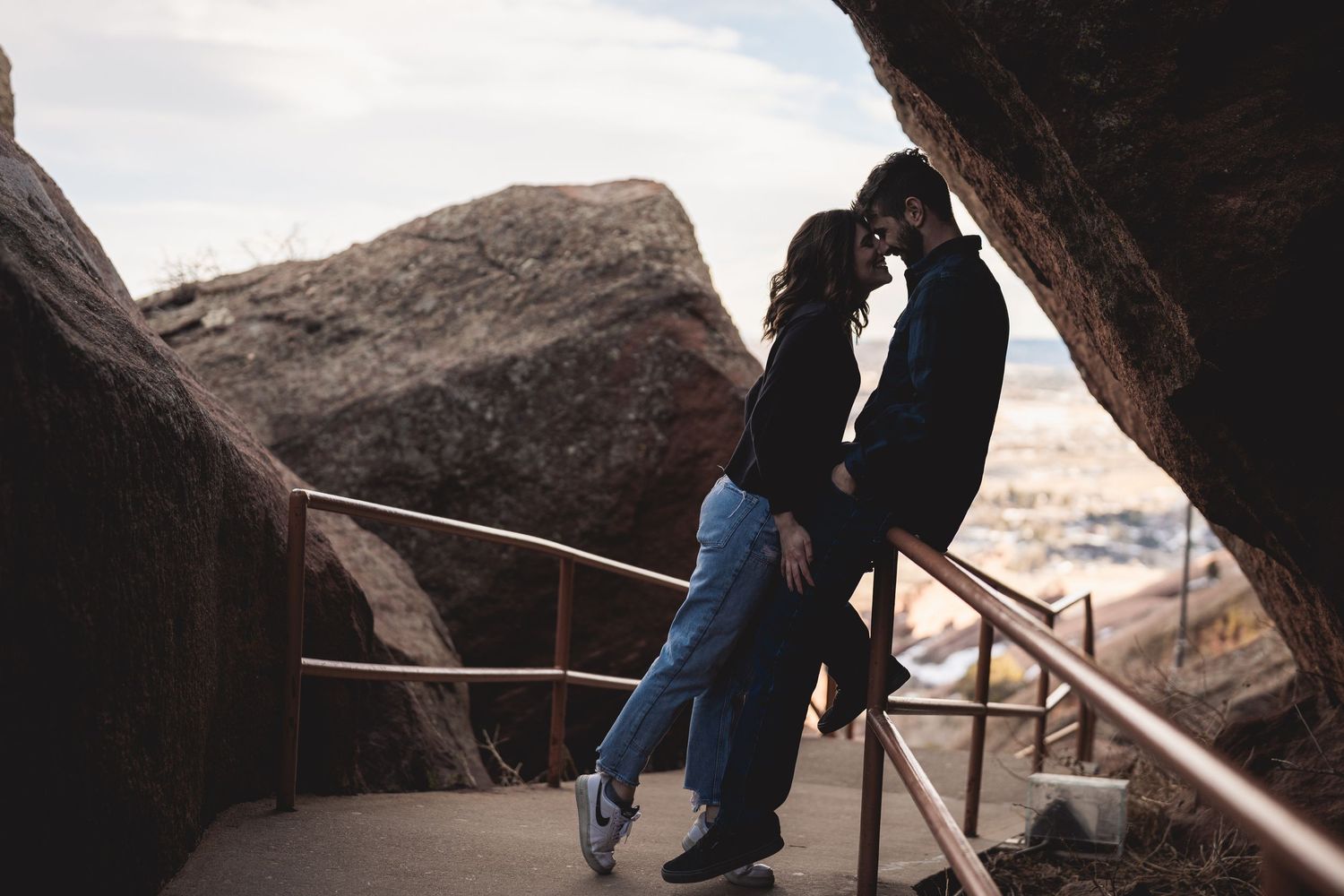 Couple sharing a romantic moment on a rocky overlook pathway, surrounded by large boulders and scenic views.